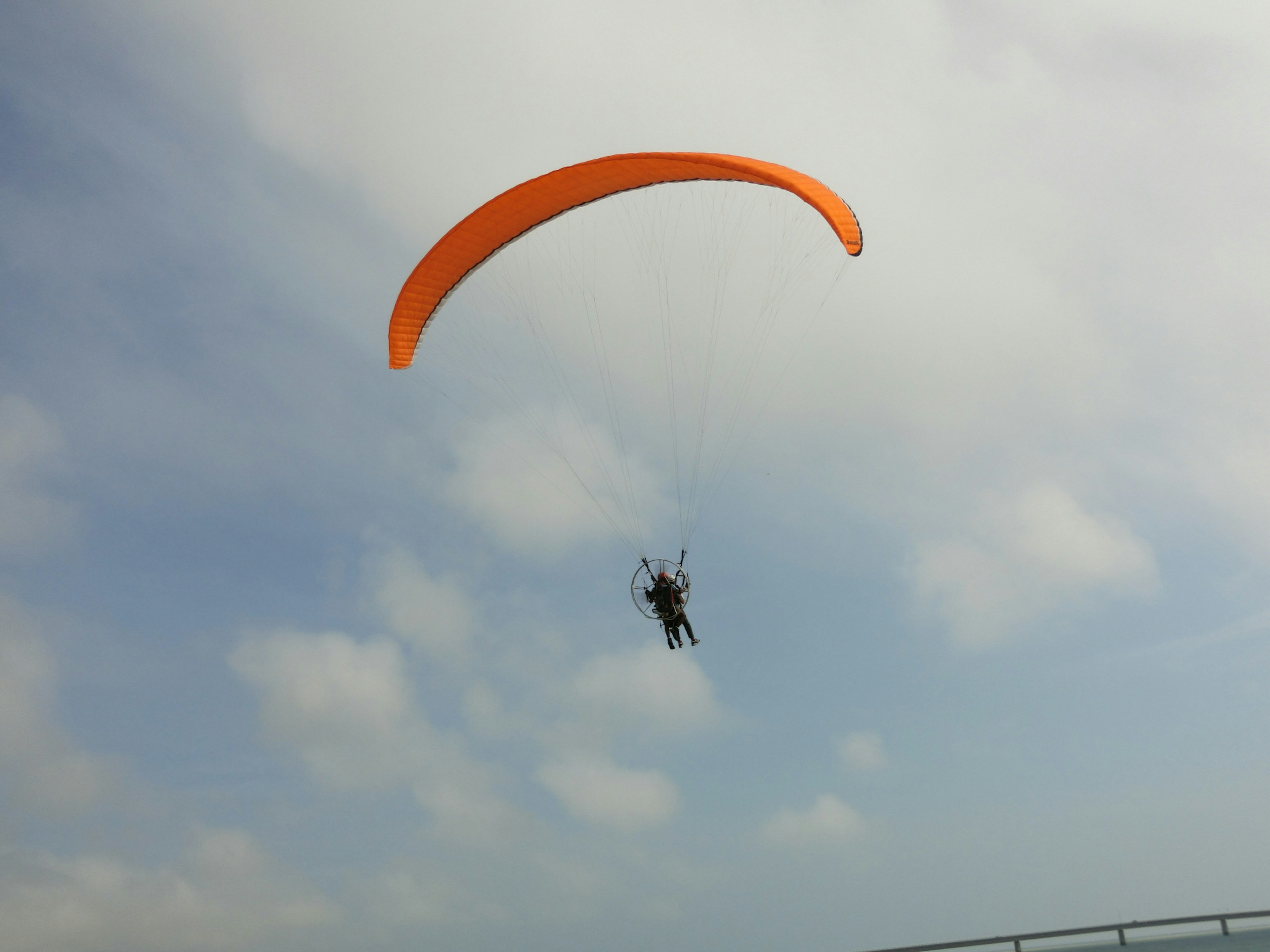 An orange paraglider soaring through the sky