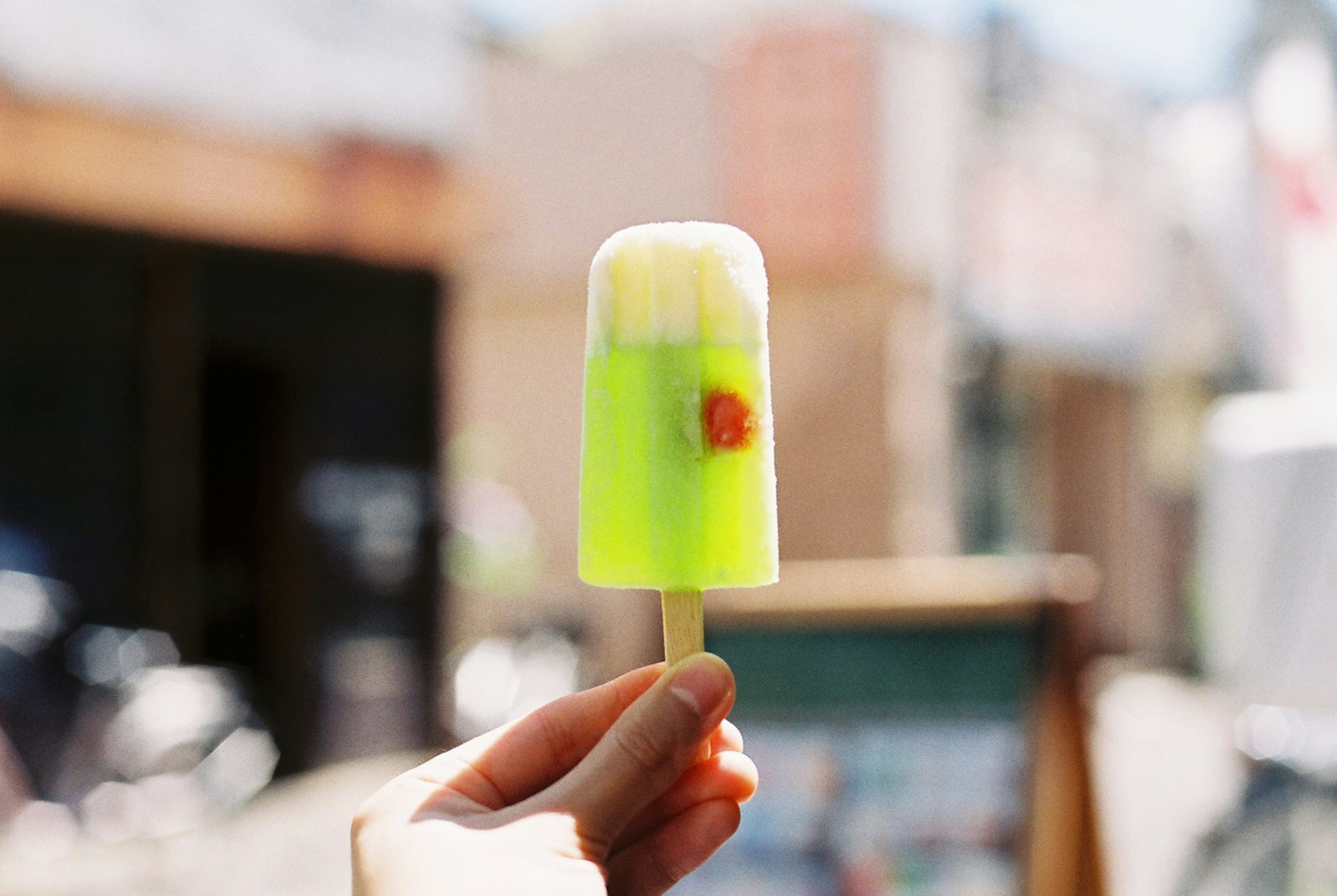 Mano sosteniendo un helado verde con una cereza encima fondo de ciudad borroso