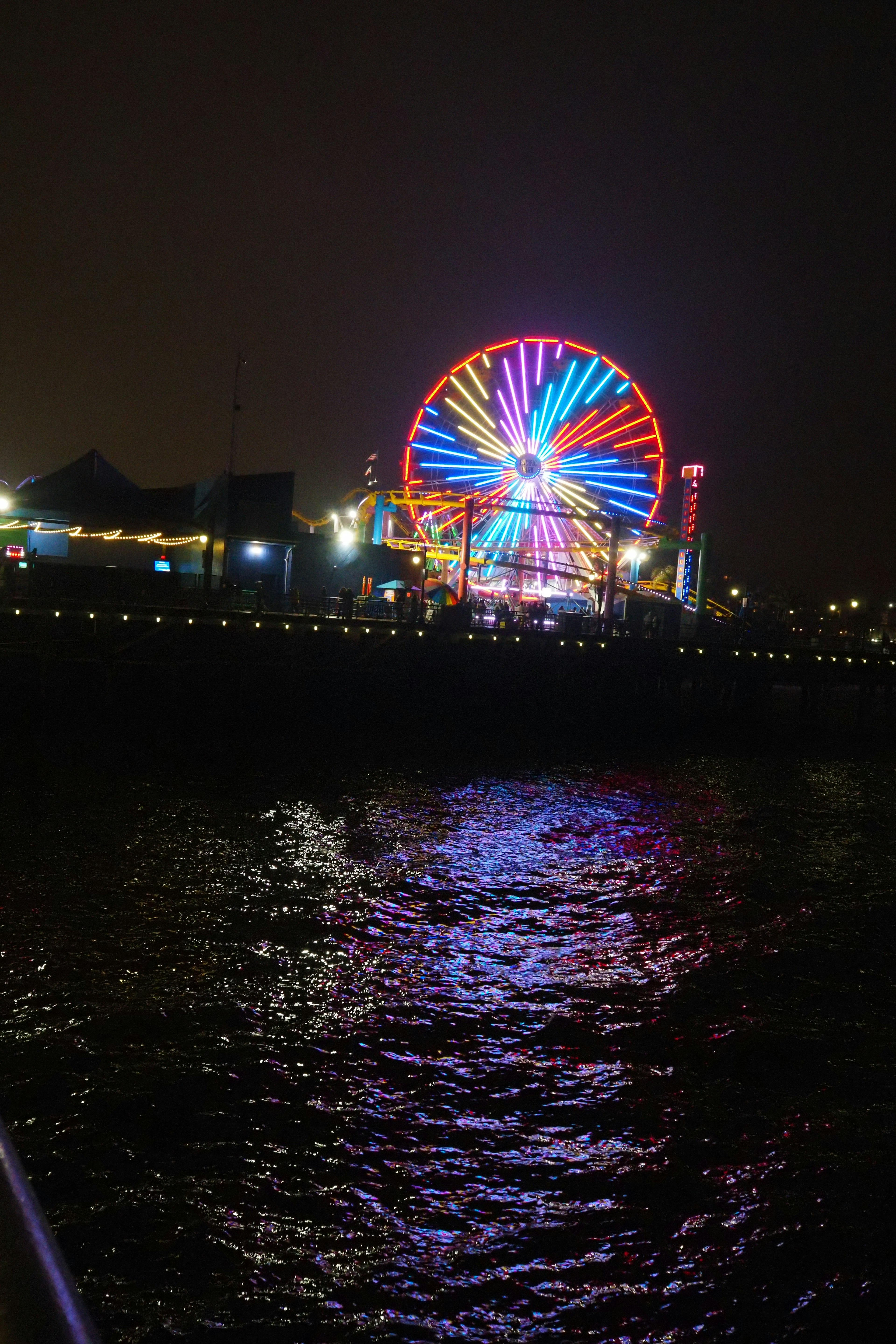 Grande roue colorée se reflétant sur l'eau la nuit