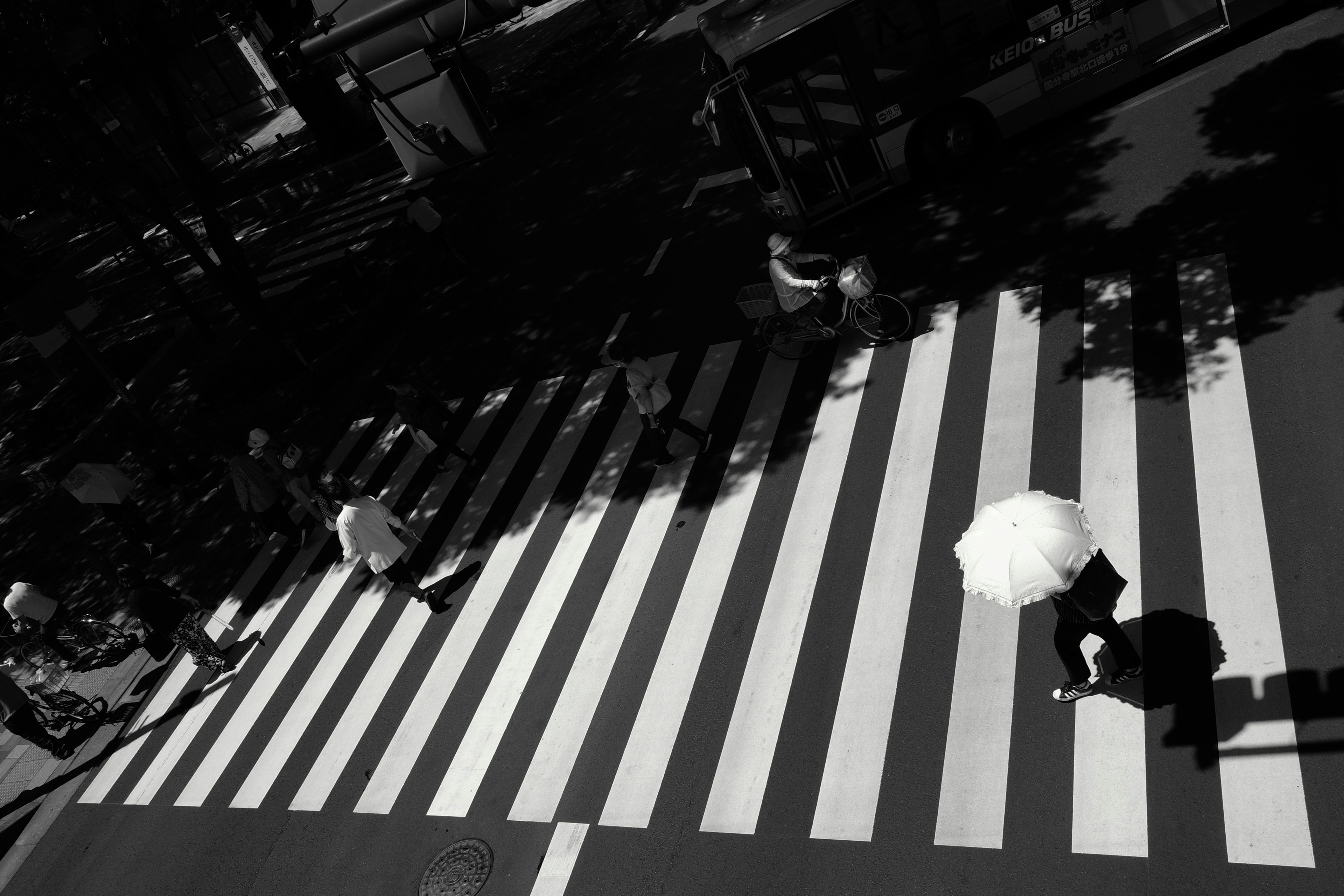 Silhouettes de personnes traversant un passage piéton noir et blanc avec une femme tenant un parasol