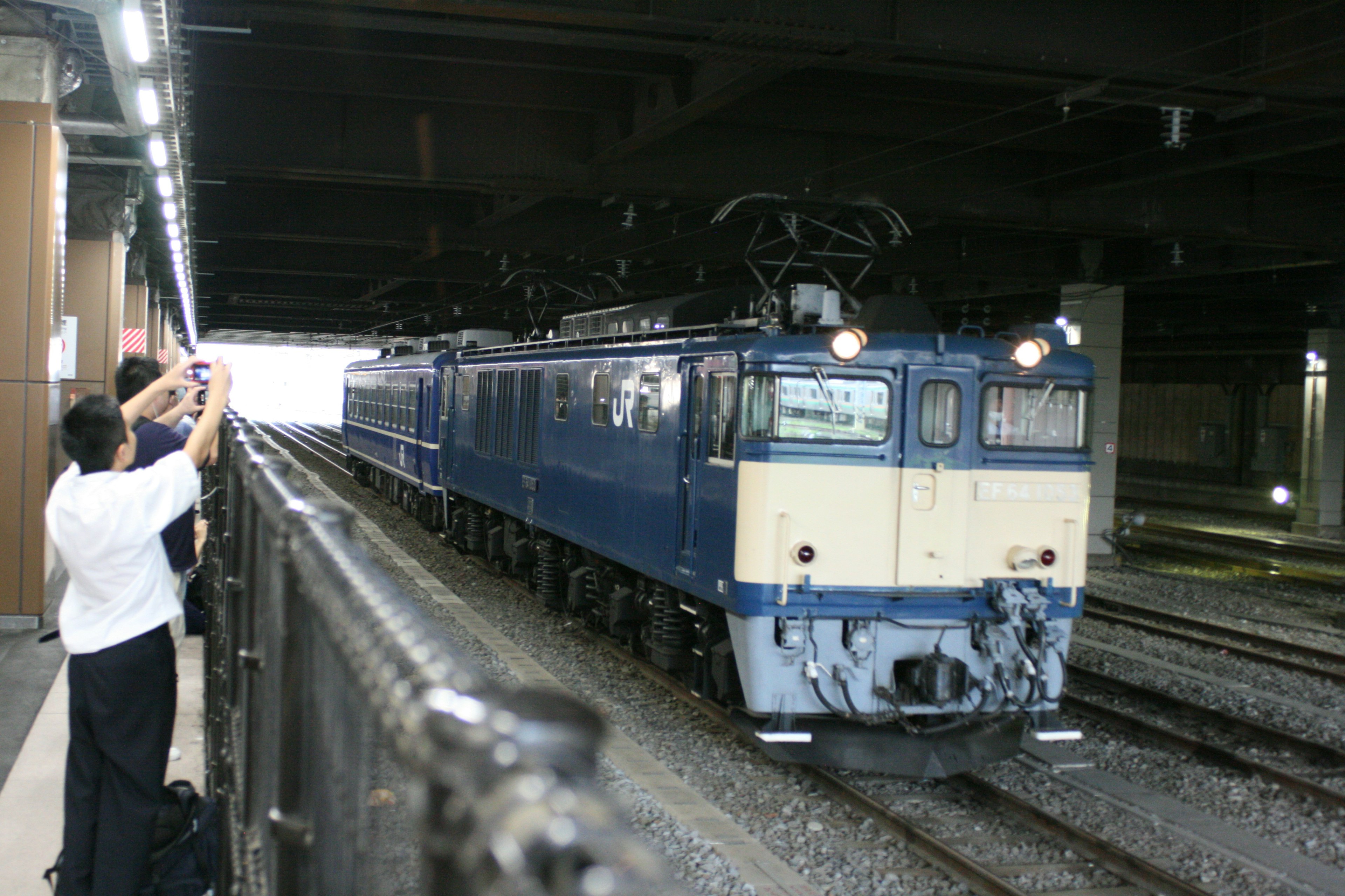 Locomotora eléctrica azul en una estación subterránea con personas tomando fotos