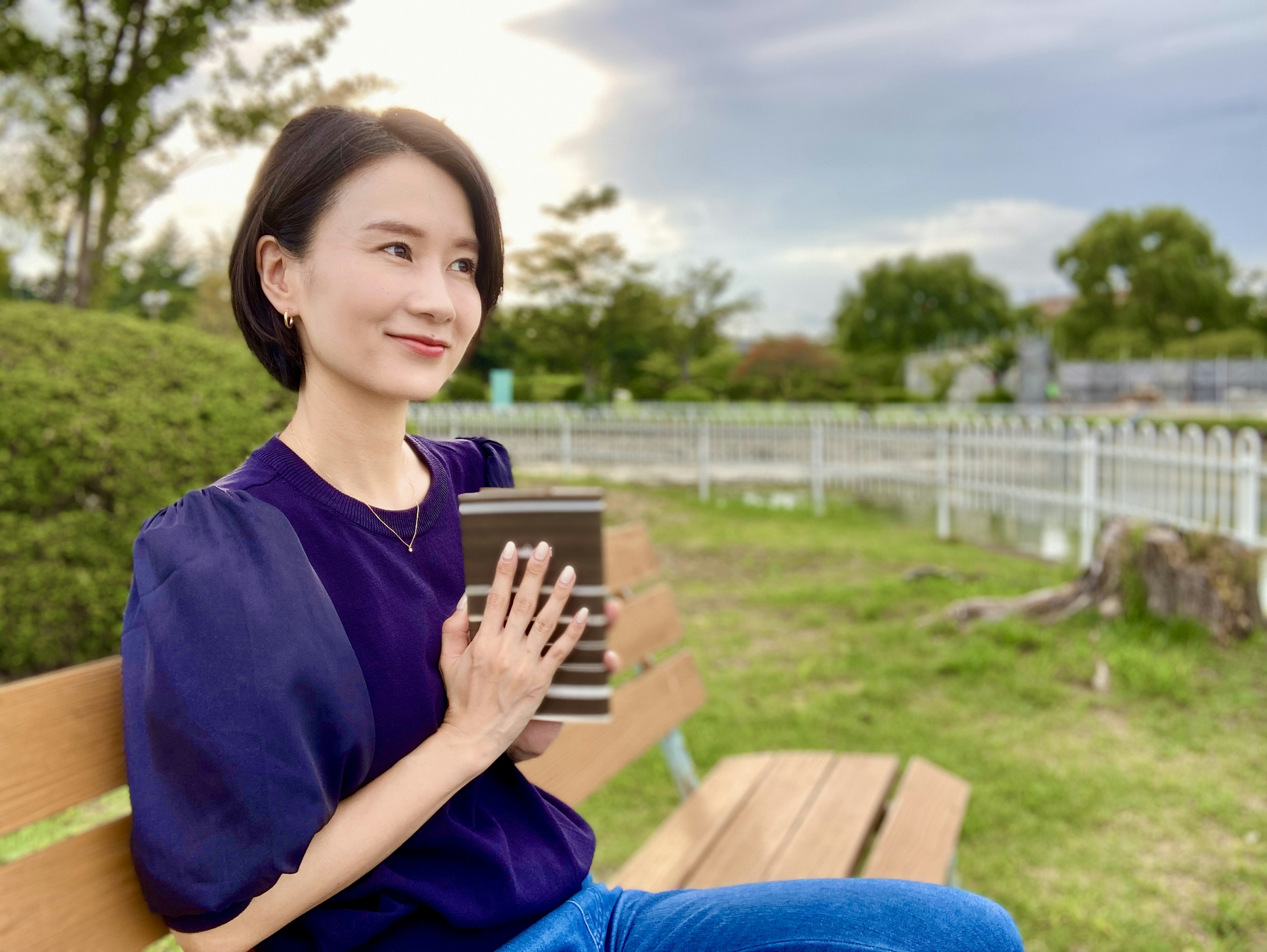 公園のベンチに座り本を持つ女性の写真