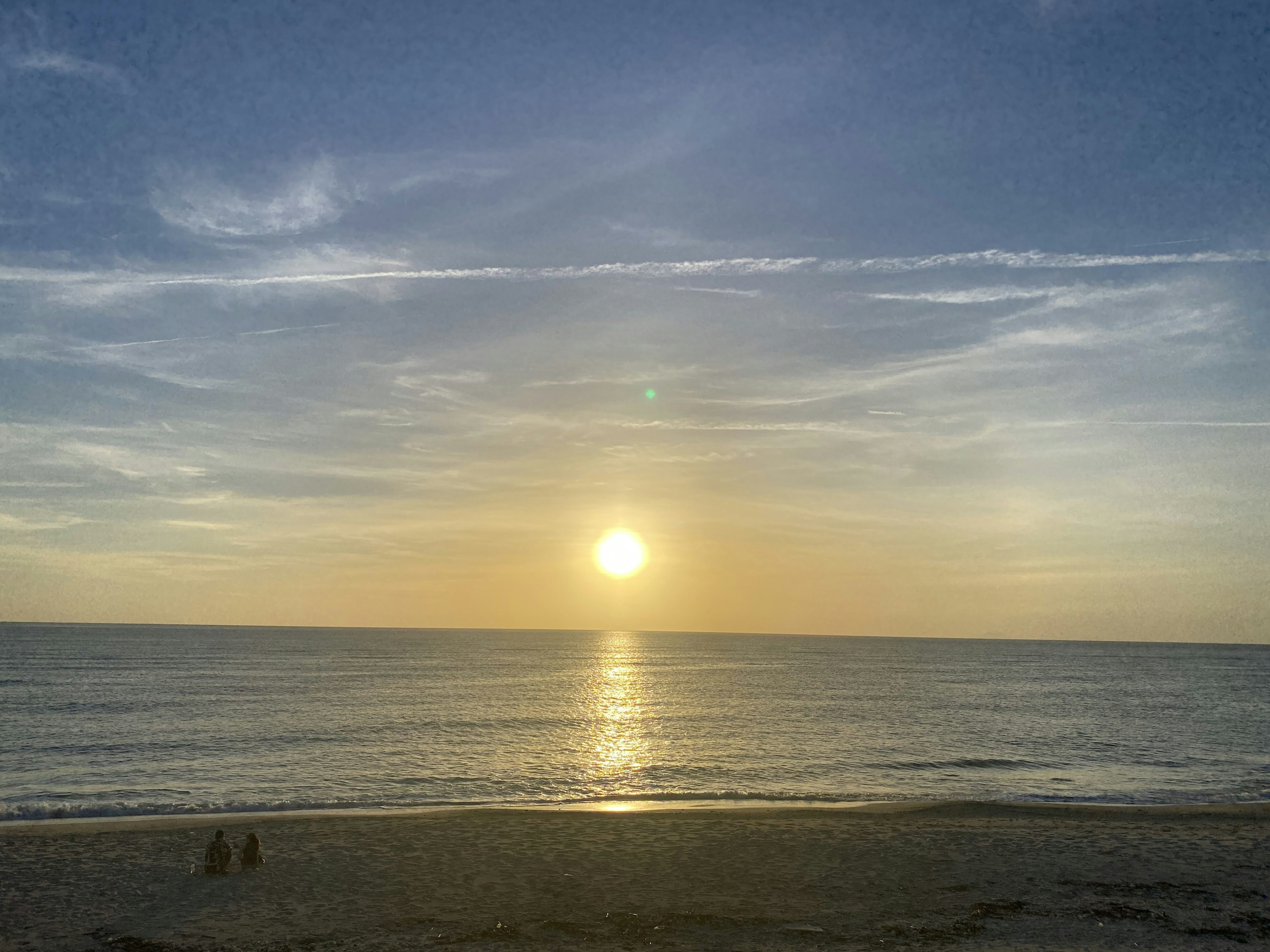 Beautiful sunset over the ocean with silhouettes of two people on the beach