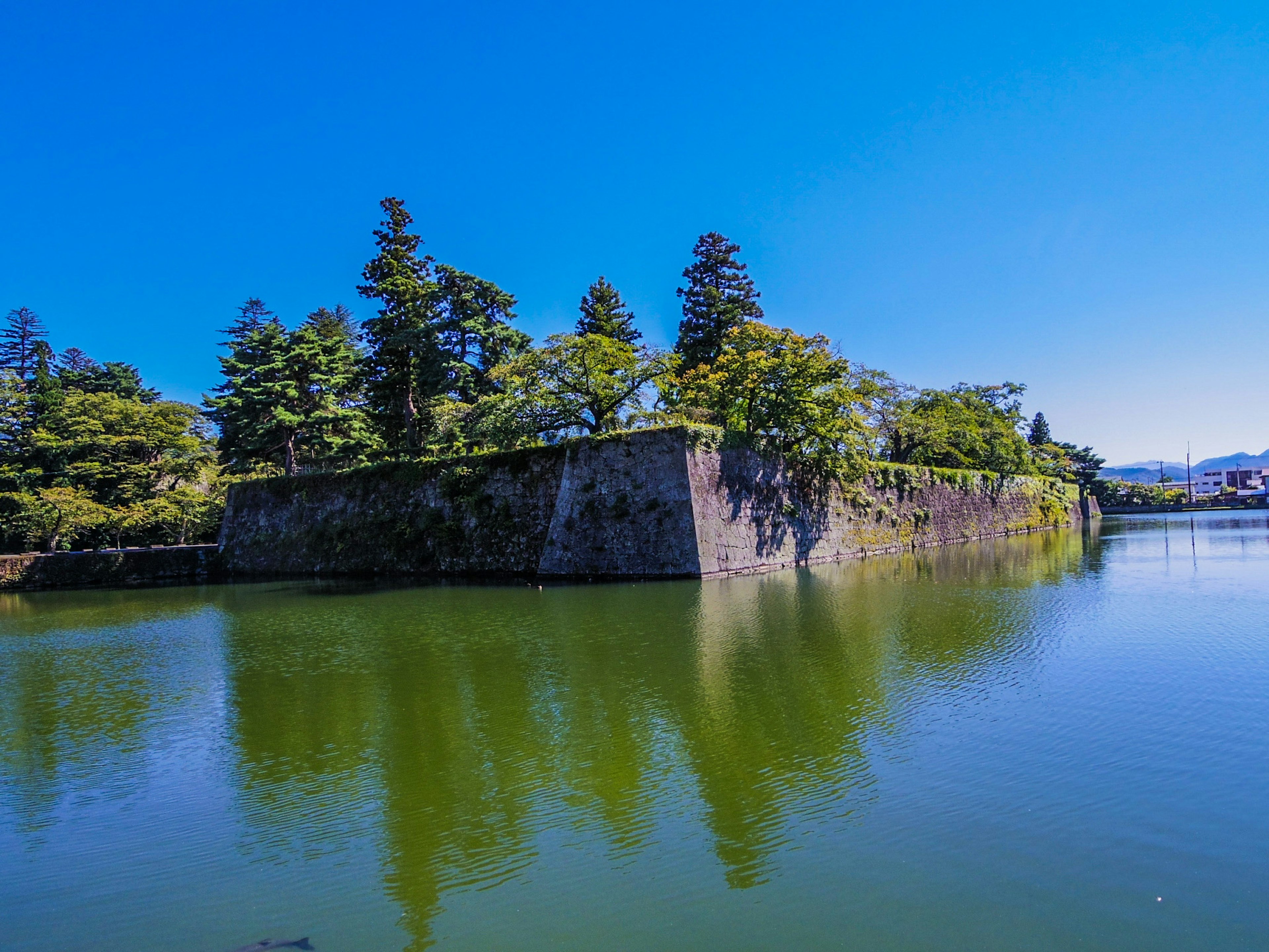 Historic stone walls reflected in green waters surrounded by trees