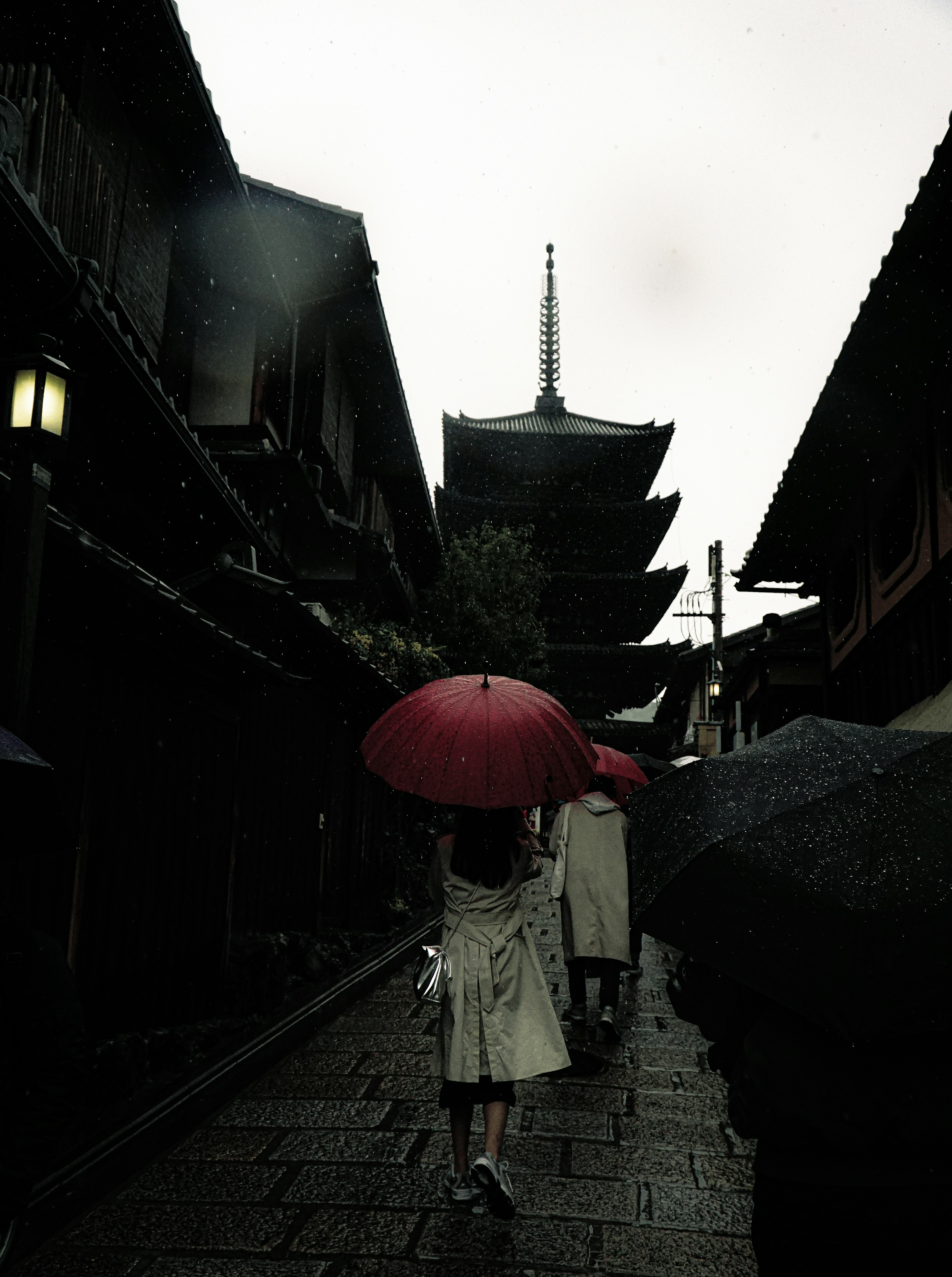 撑着红伞的女人在雨中走过传统建筑