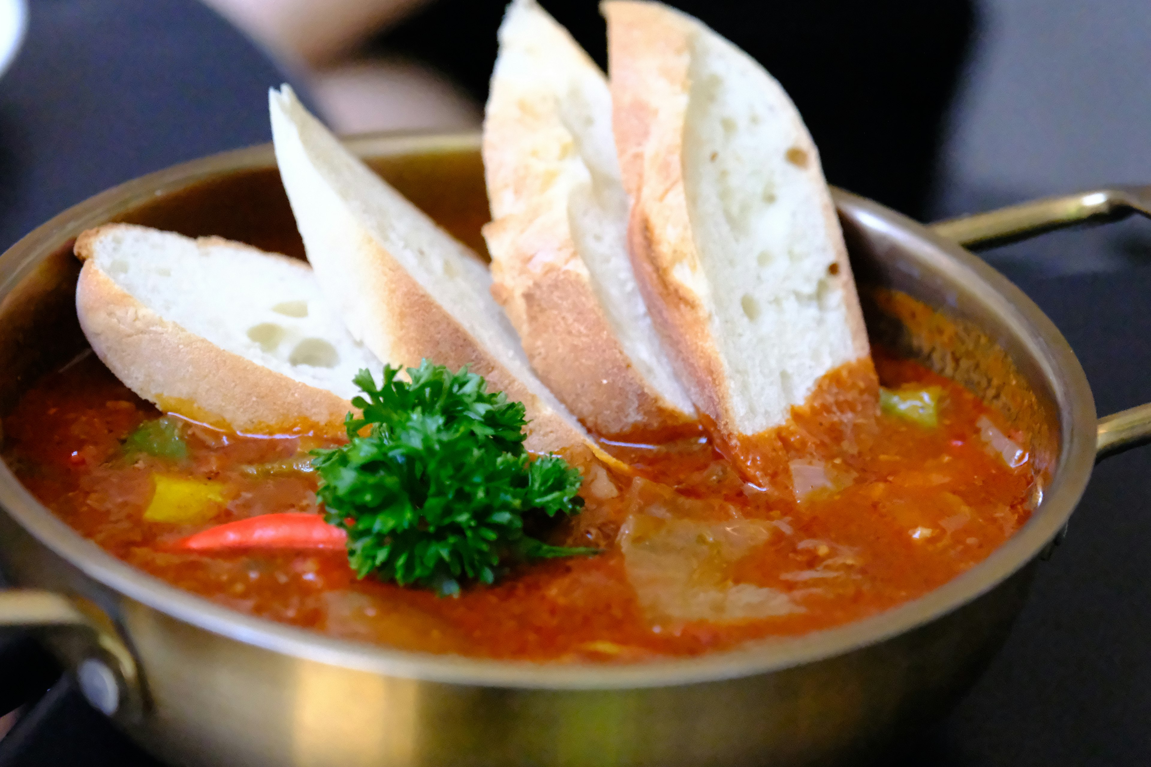 A pot of soup with slices of bread and a sprig of parsley