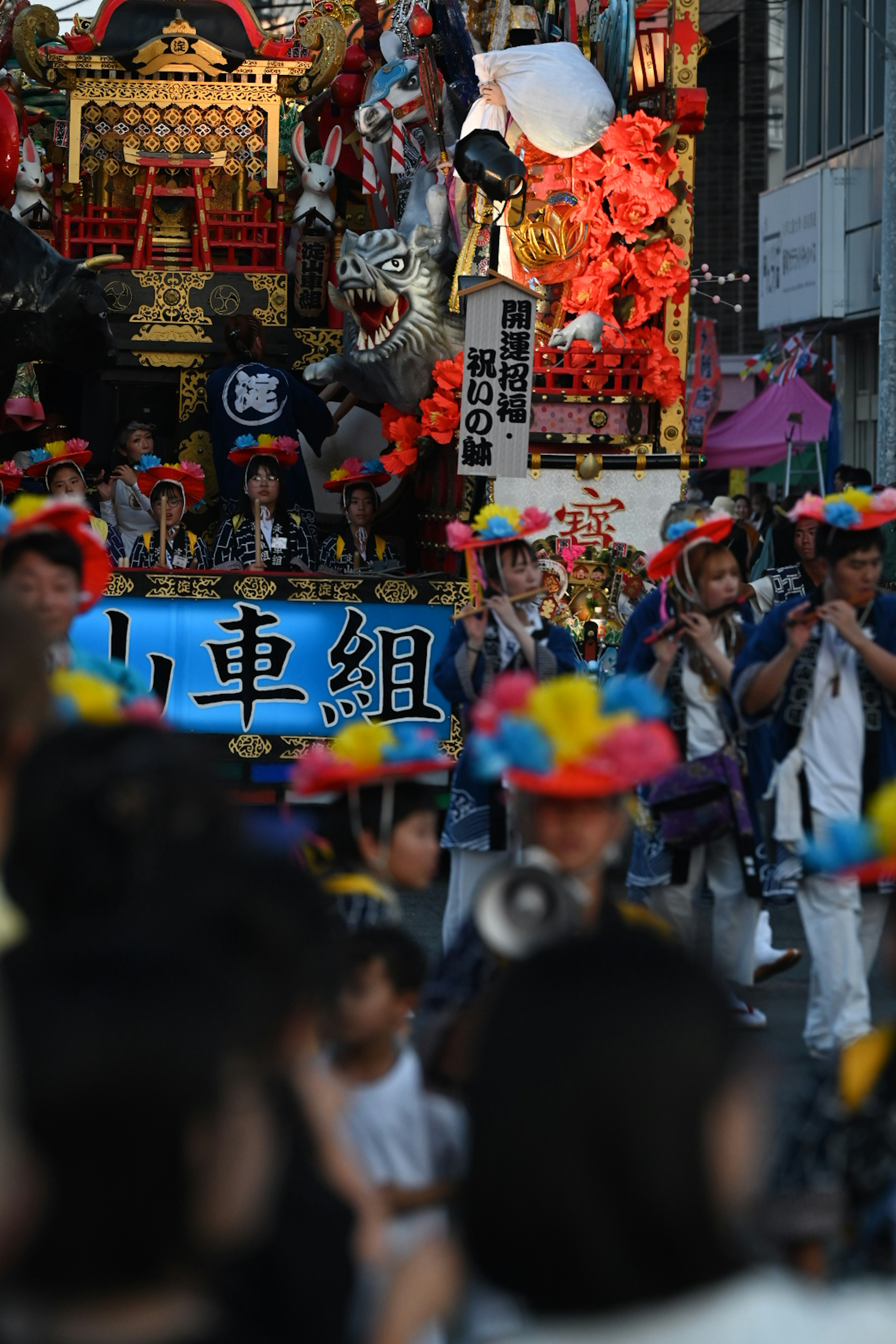 Festival participants wearing colorful hats gather in front of a large float