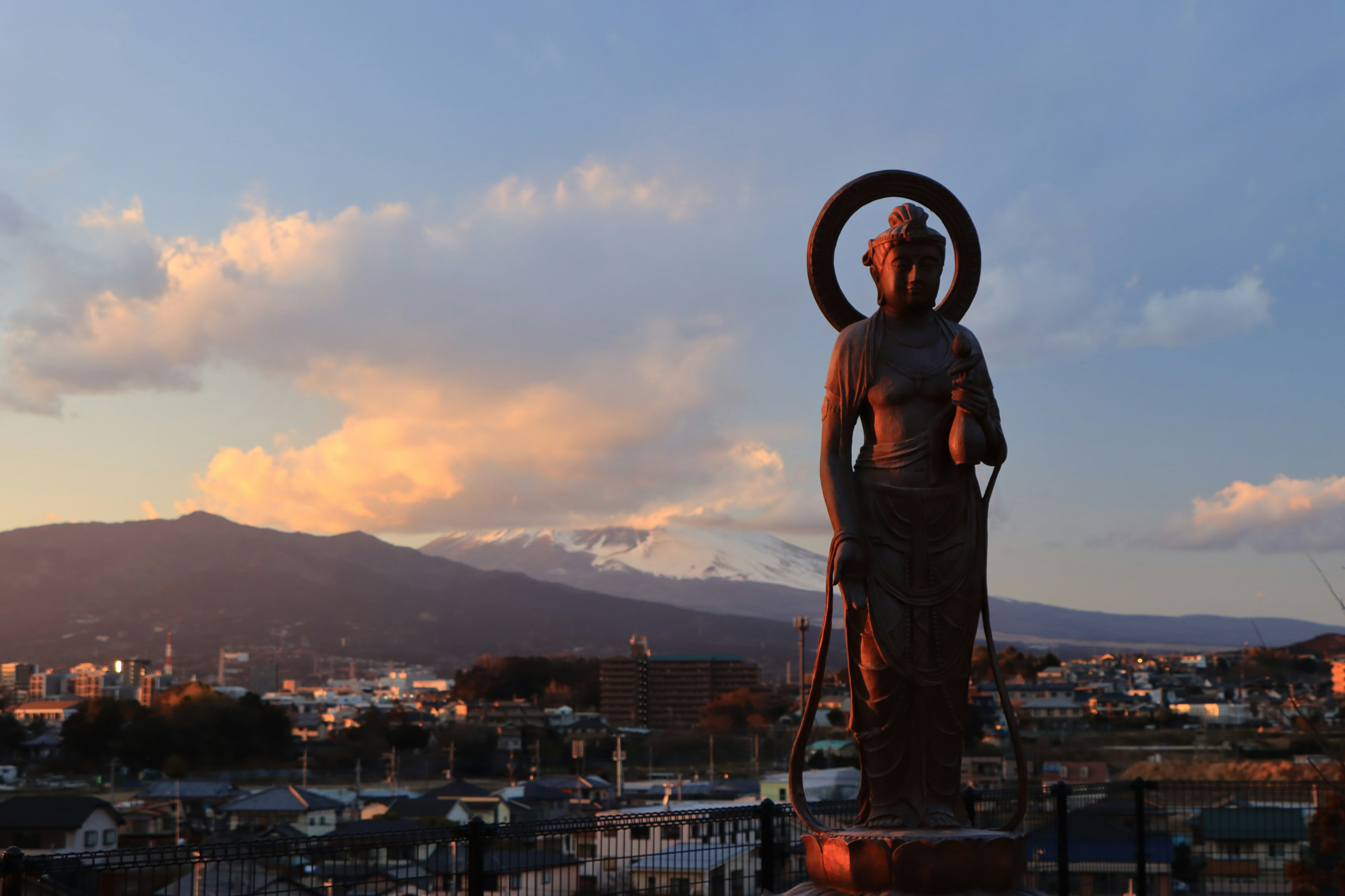 Silhouette of a statue against a sunset sky with cityscape in the background