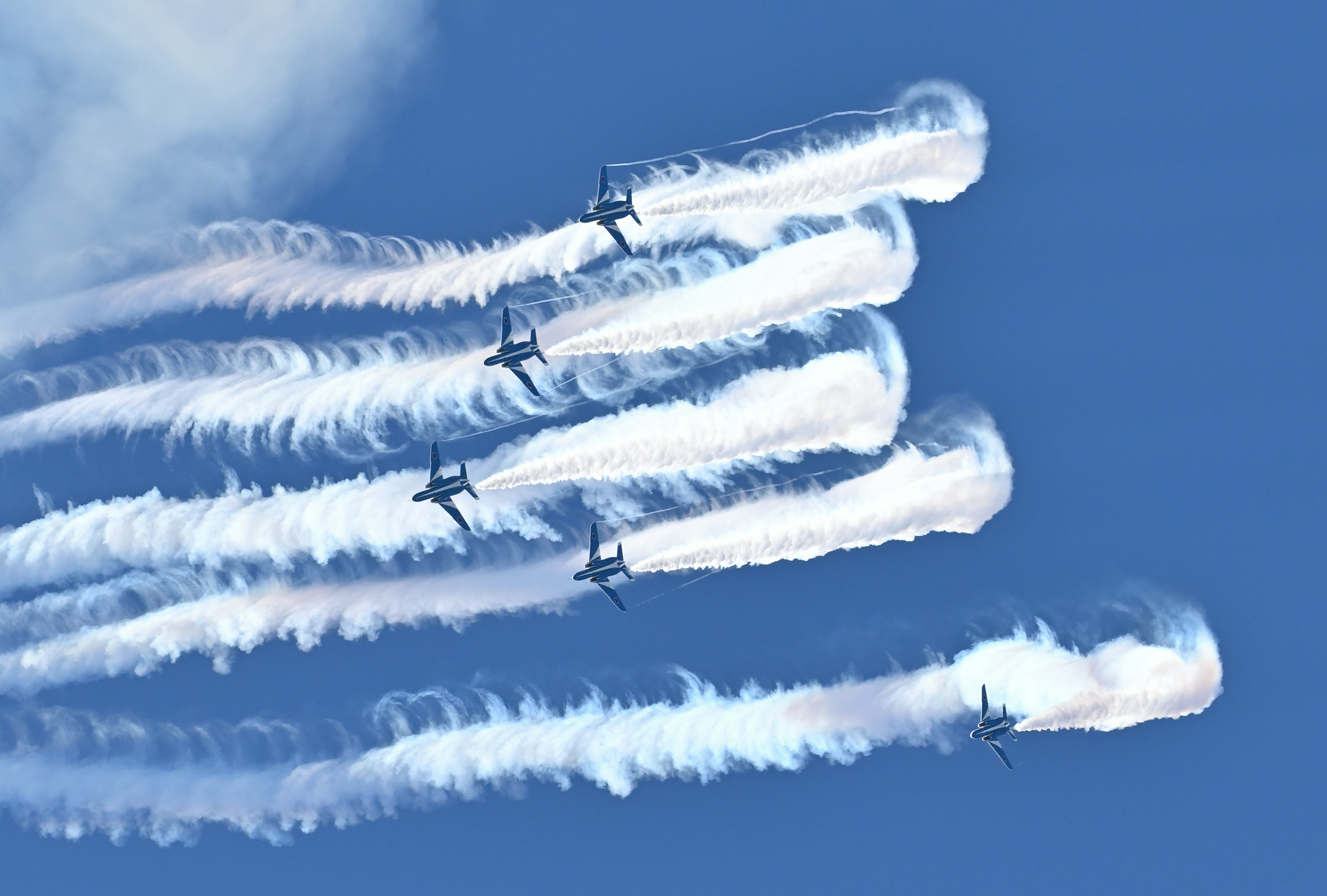 Multiple aircraft flying in formation with smoke trails against a blue sky