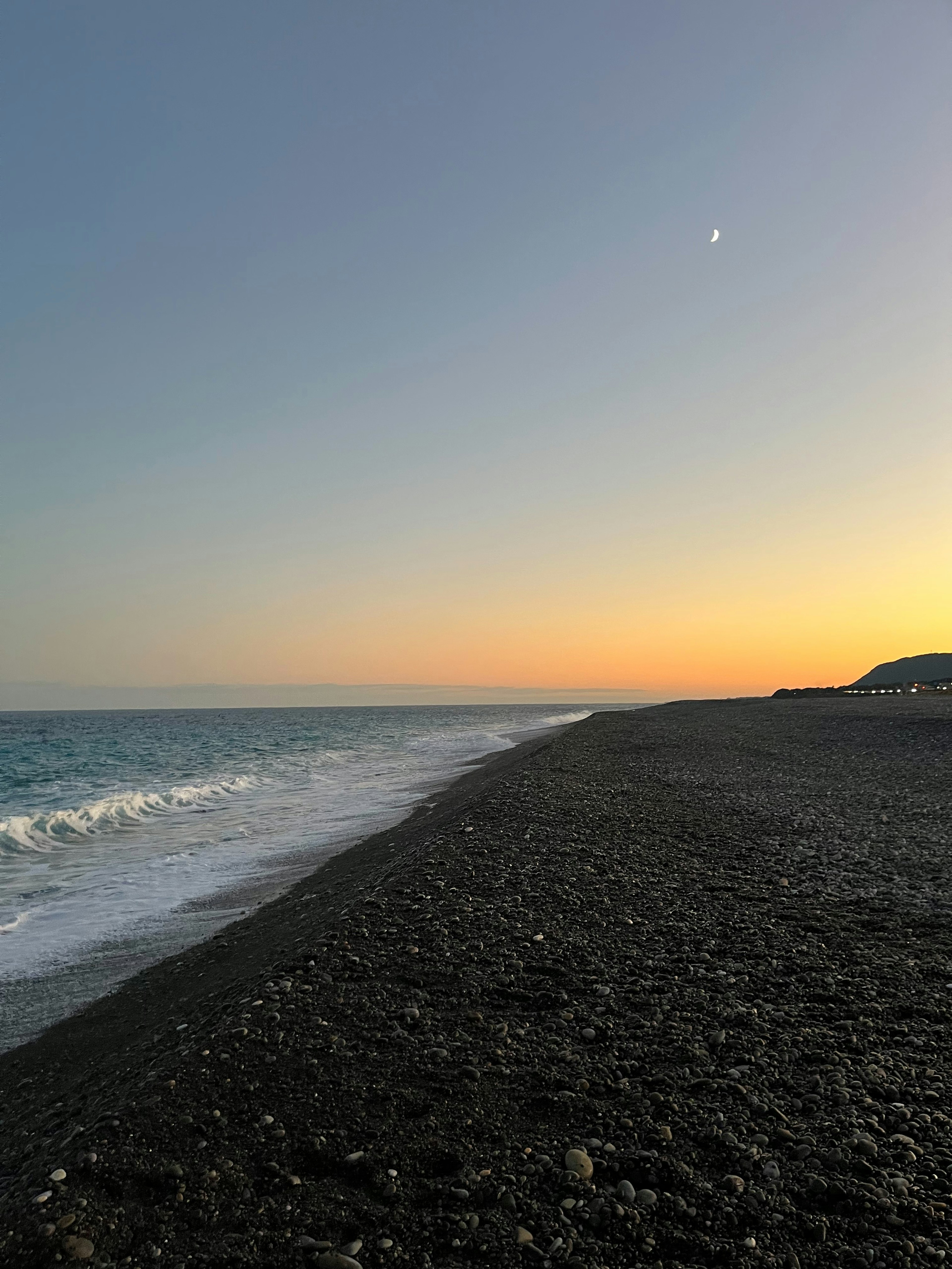 Kiesstrand bei Sonnenuntergang mit sanften Wellen und klarem Himmel