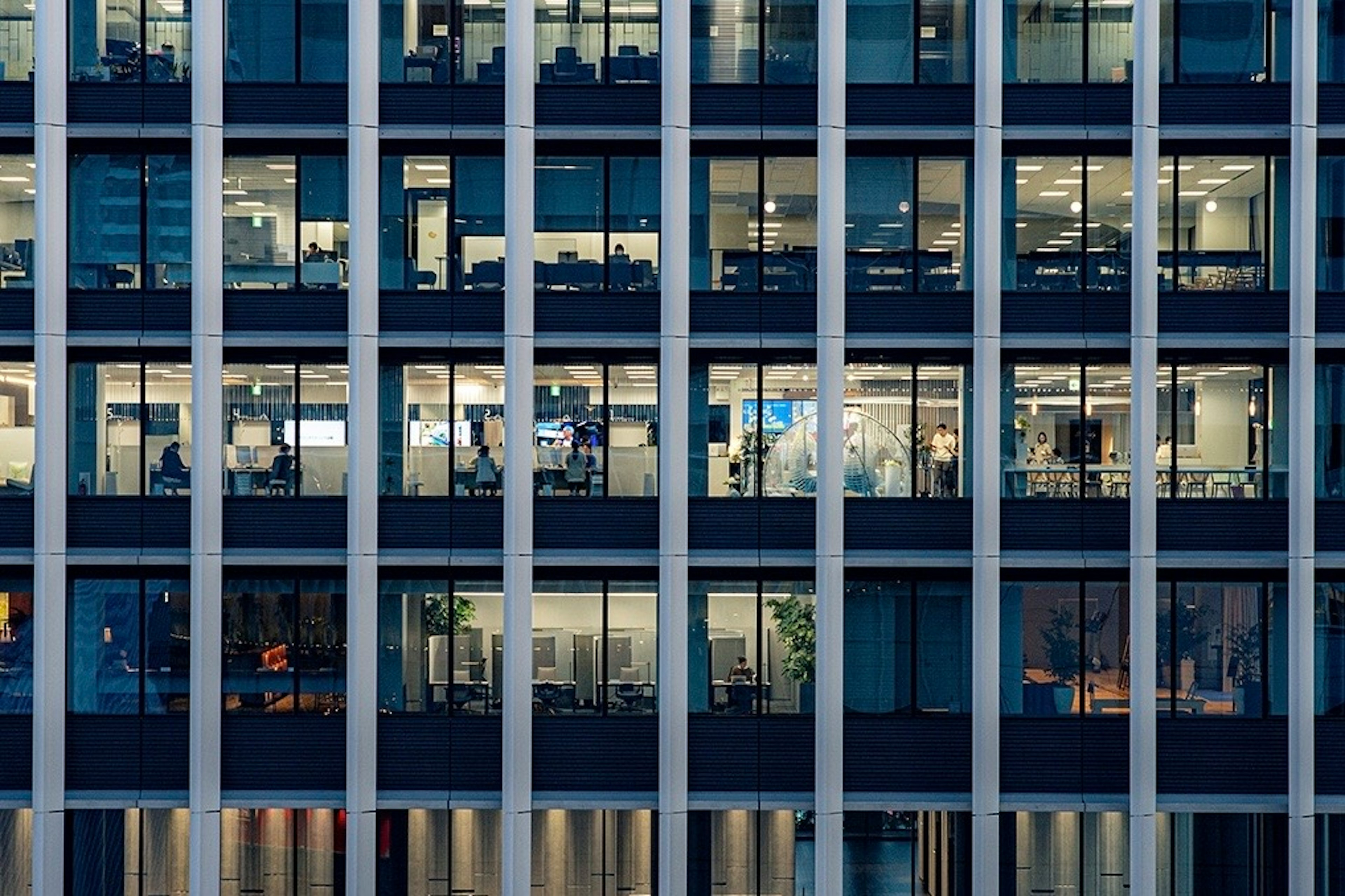 Façade d'un immeuble de bureaux avec des fenêtres éclairées montrant des personnes travaillant