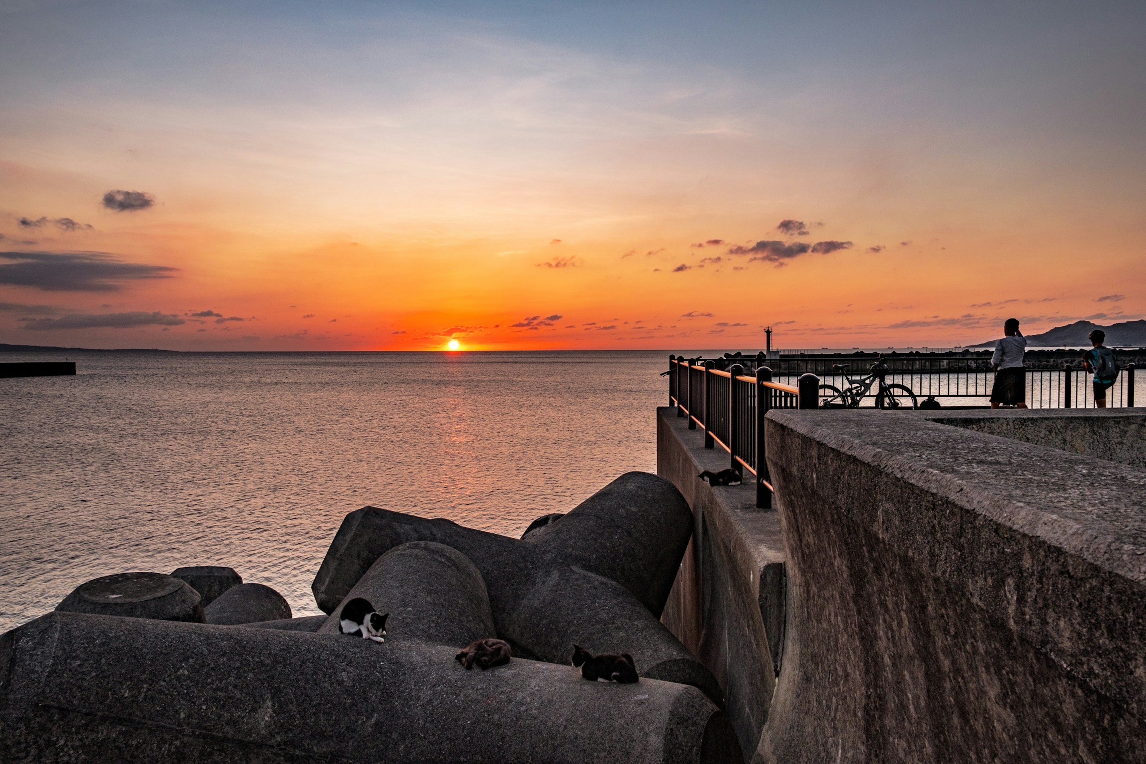 Sunset over the ocean with a pier and rocks in the foreground