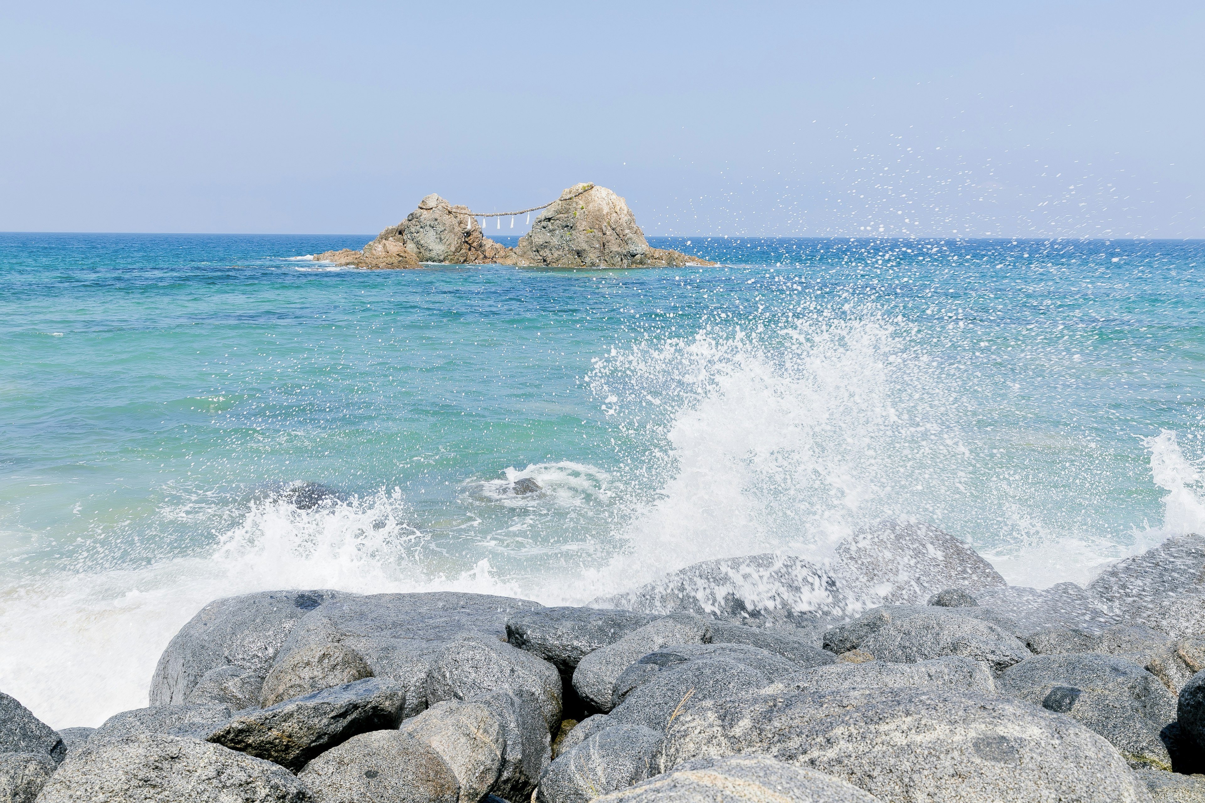 岩石海岸，浪花四溅，远处是清澈蓝色海洋中的小岛