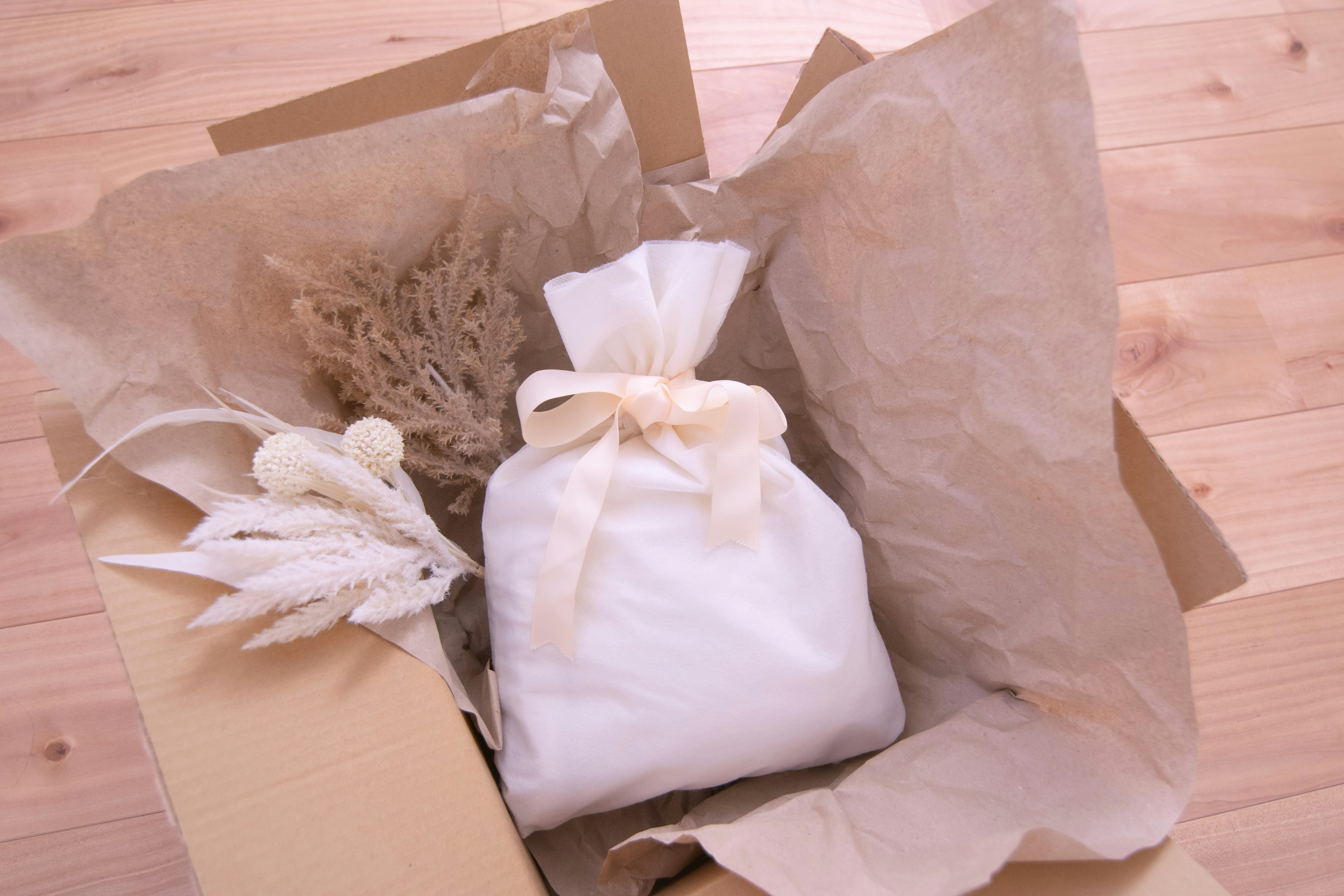 Open box containing a gift wrapped in white fabric and dried plant decorations