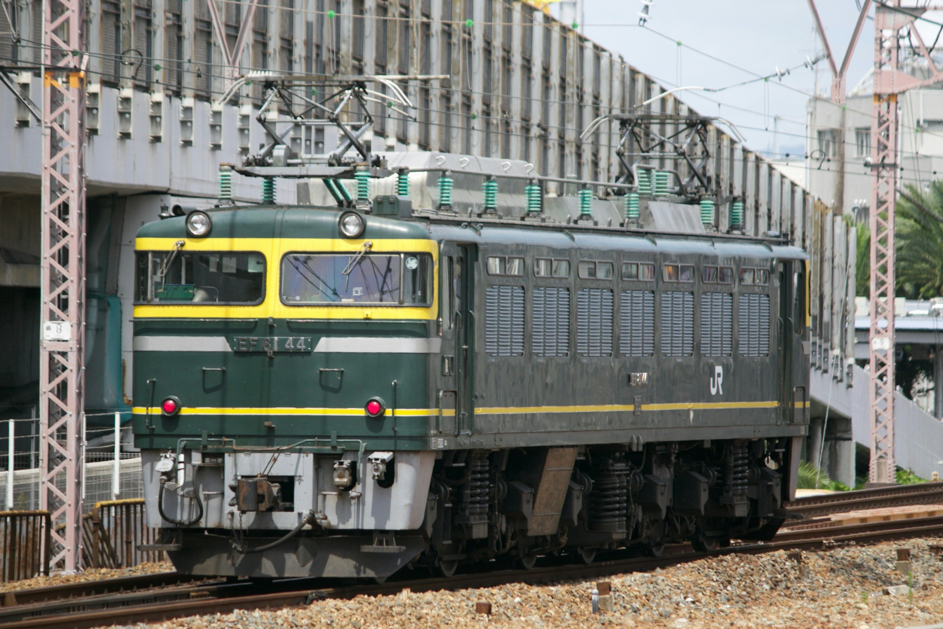 緑と黄色の塗装の電気機関車が線路を走っている風景