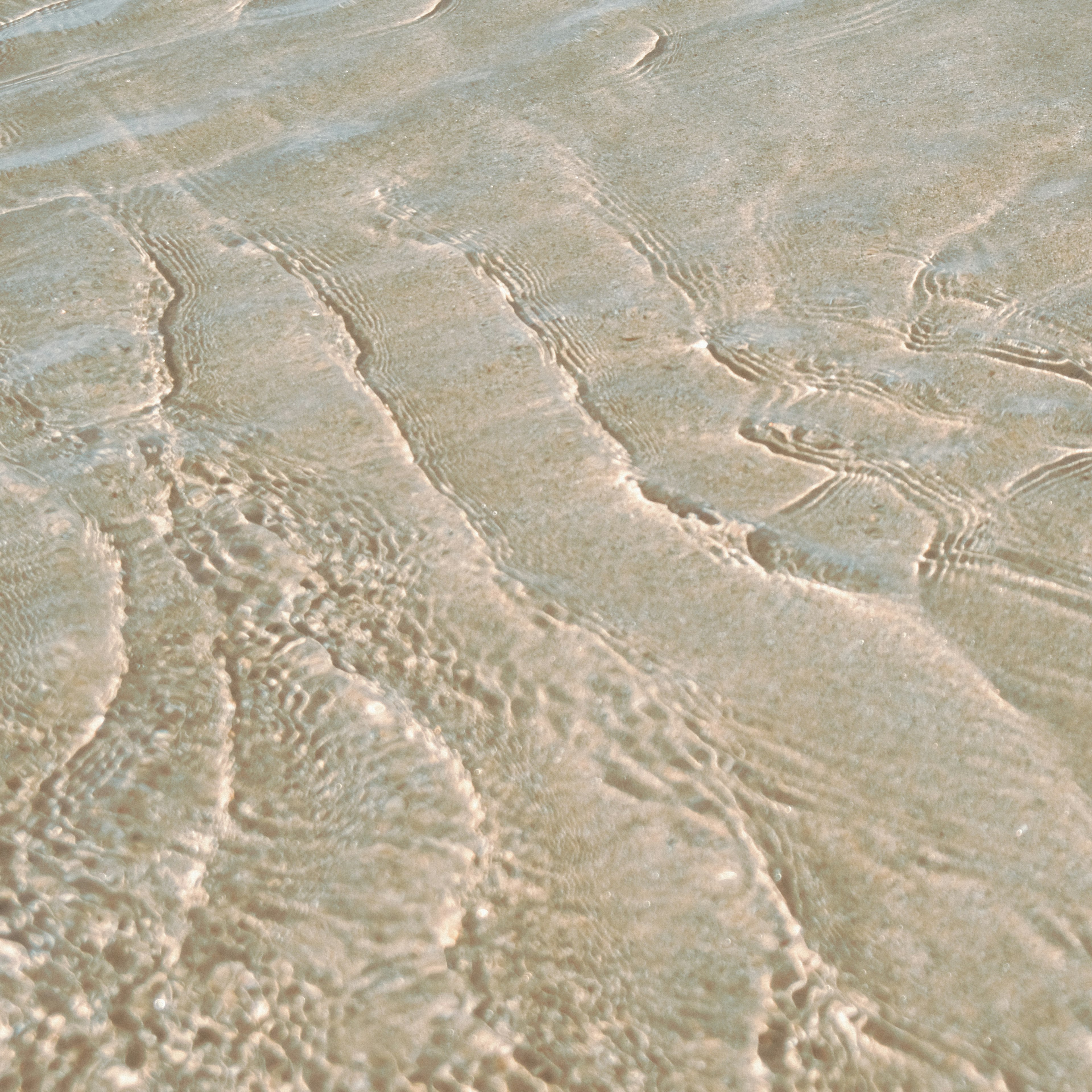 Wellige Wasseroberfläche, die darunter liegende Sandmuster zeigt