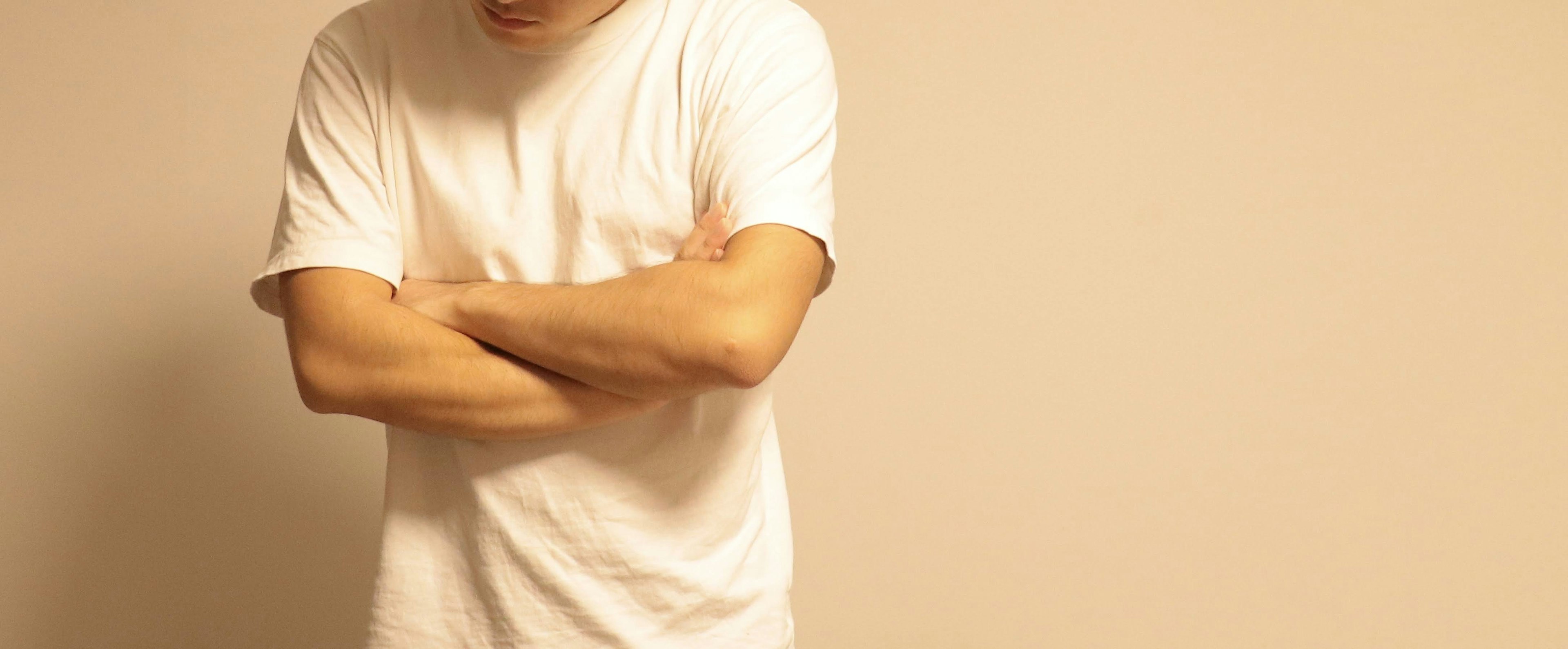 Un homme en t-shirt blanc avec les bras croisés se tenant devant un fond beige