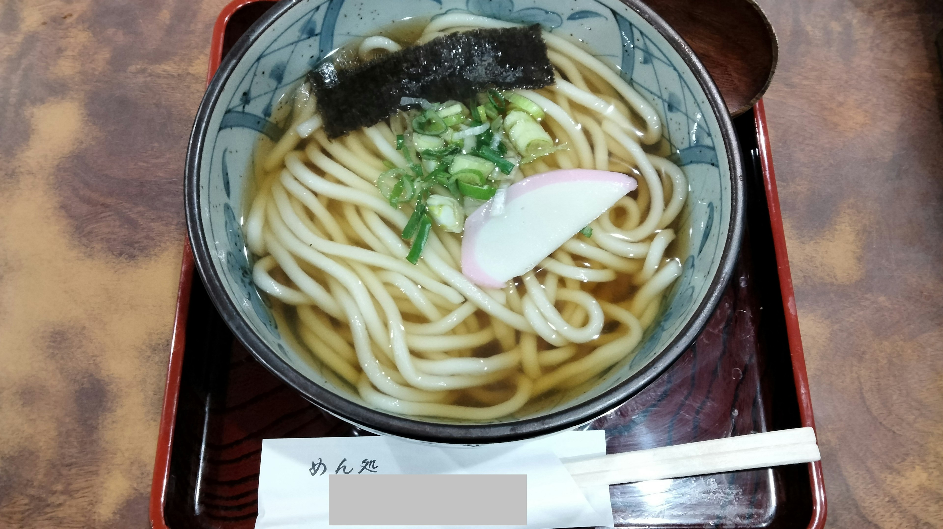 Mangkuk mie udon dengan taburan daun bawang dan kamaboko dalam gaya Jepang tradisional