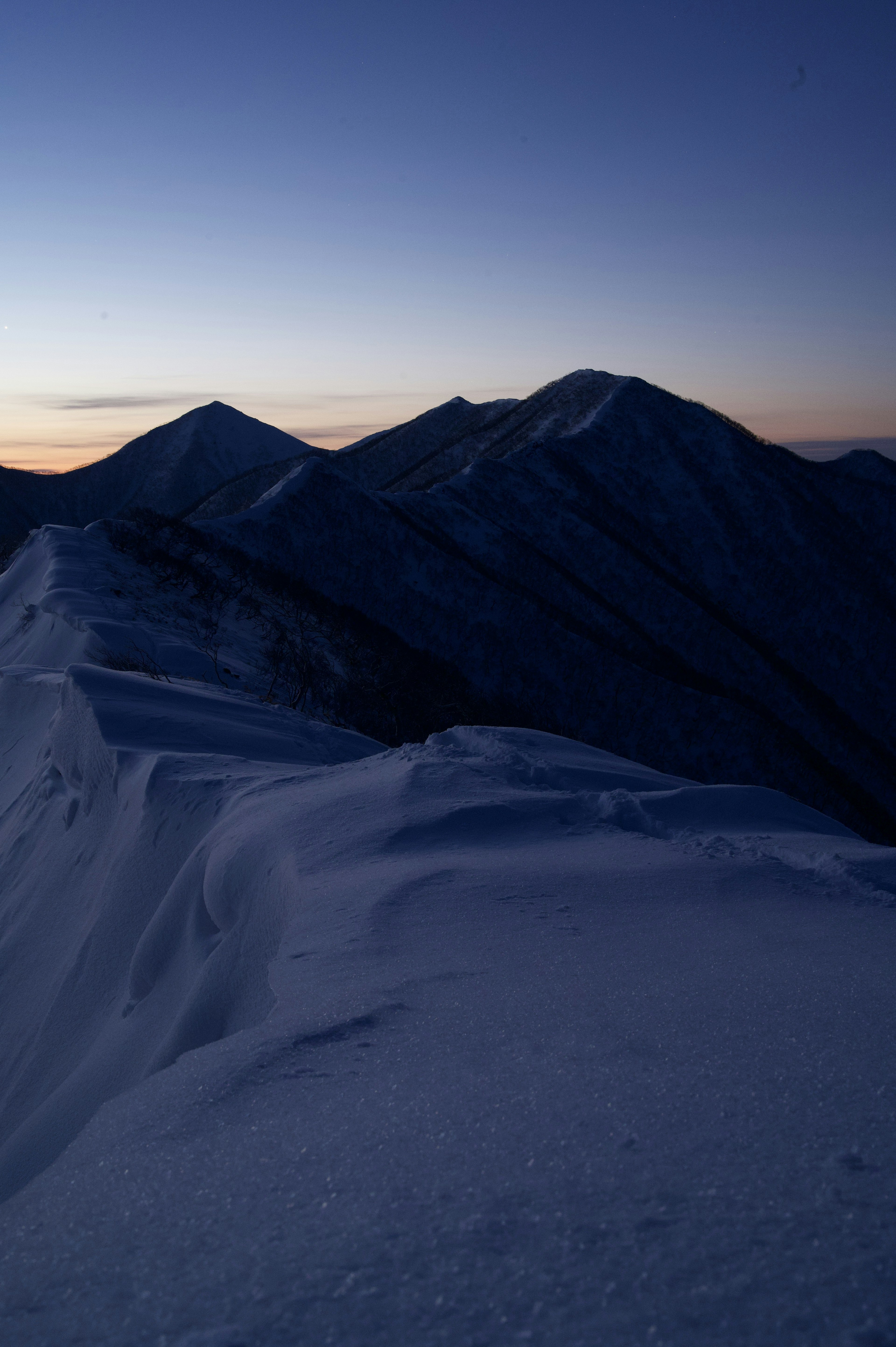 Silhouette di montagne innevate contro un cielo al crepuscolo