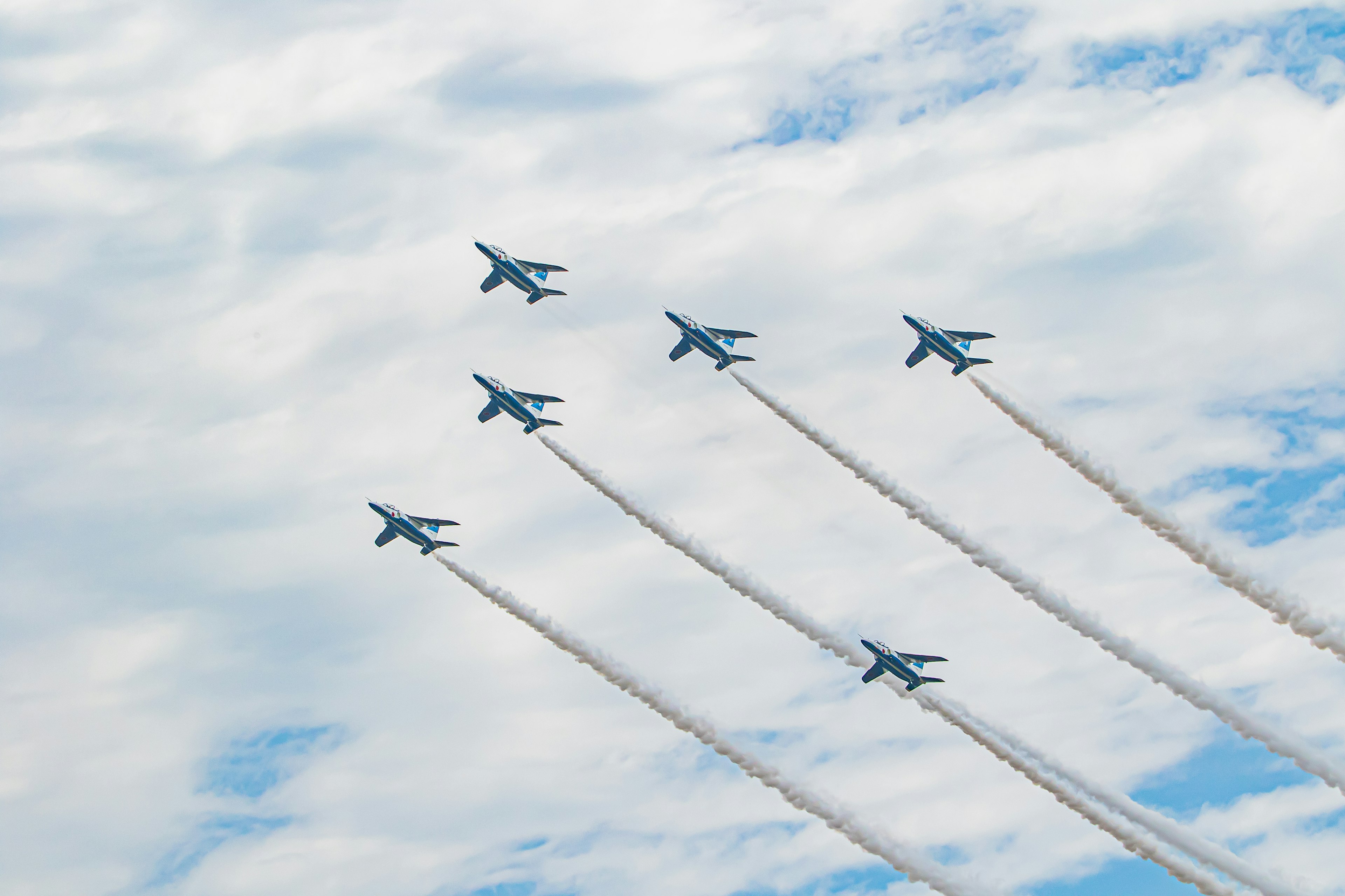 Blaue Militärjets fliegen in Formation vor einem bewölkten Himmel