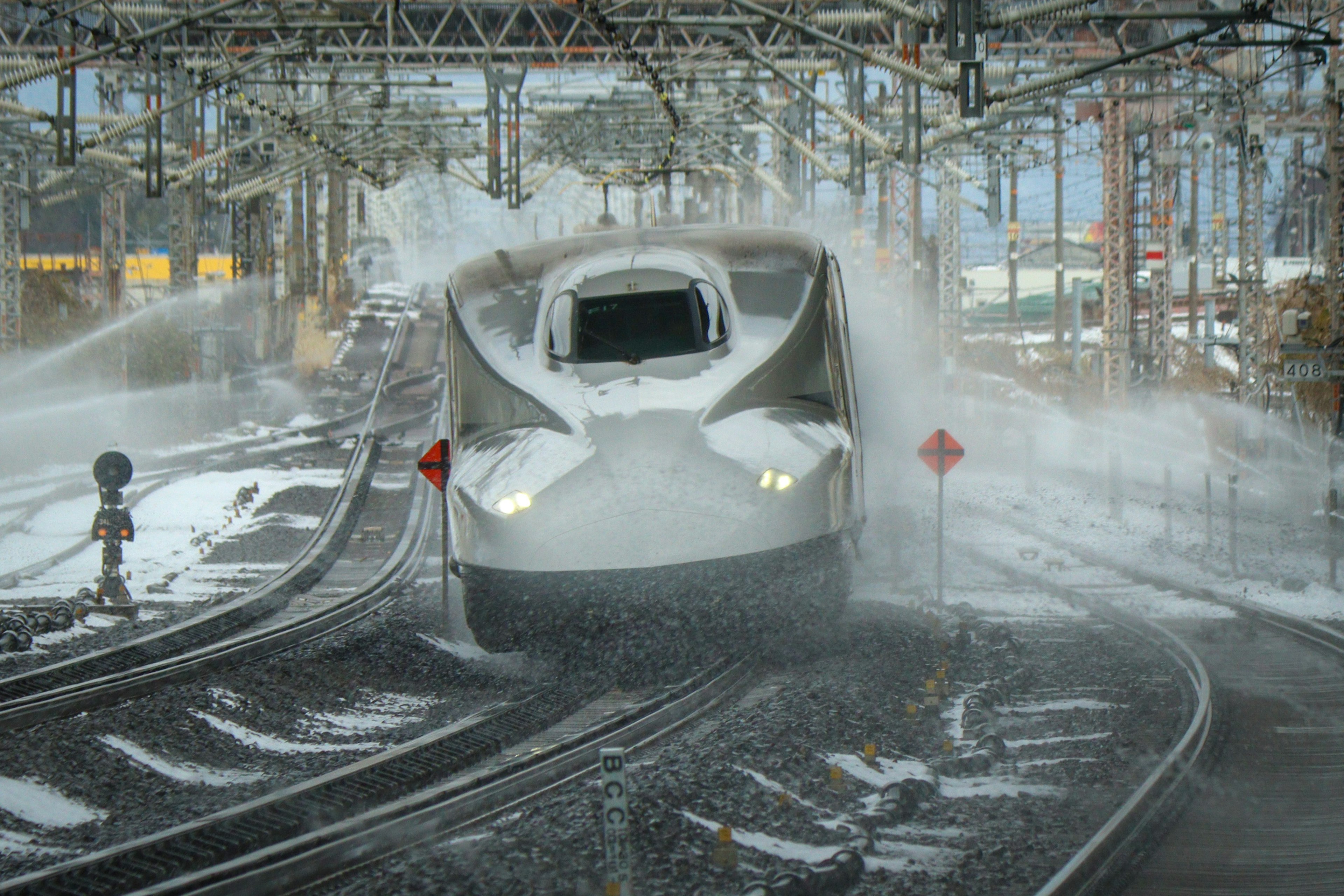 Mit Schnee bedeckter Shinkansen-Zug, der am Bahnhof ankommt und Schnee spritzt