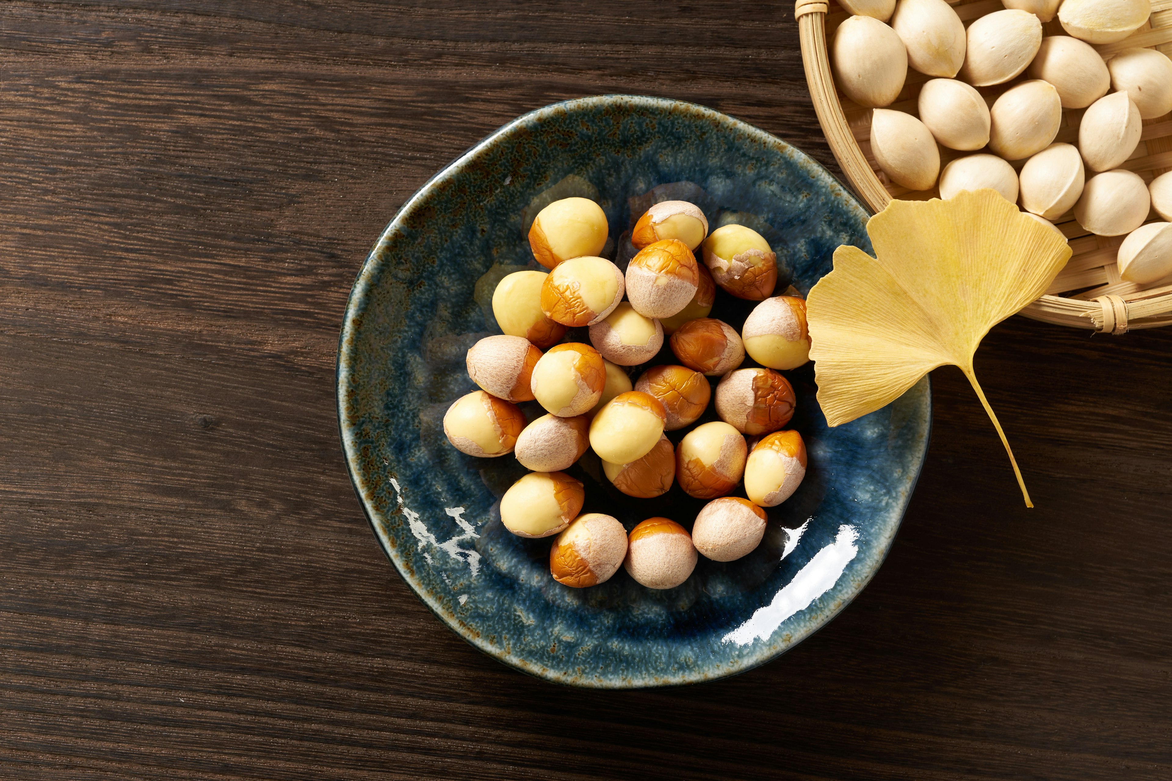 Kacang ginkgo berwarna di piring biru dengan daun ginkgo