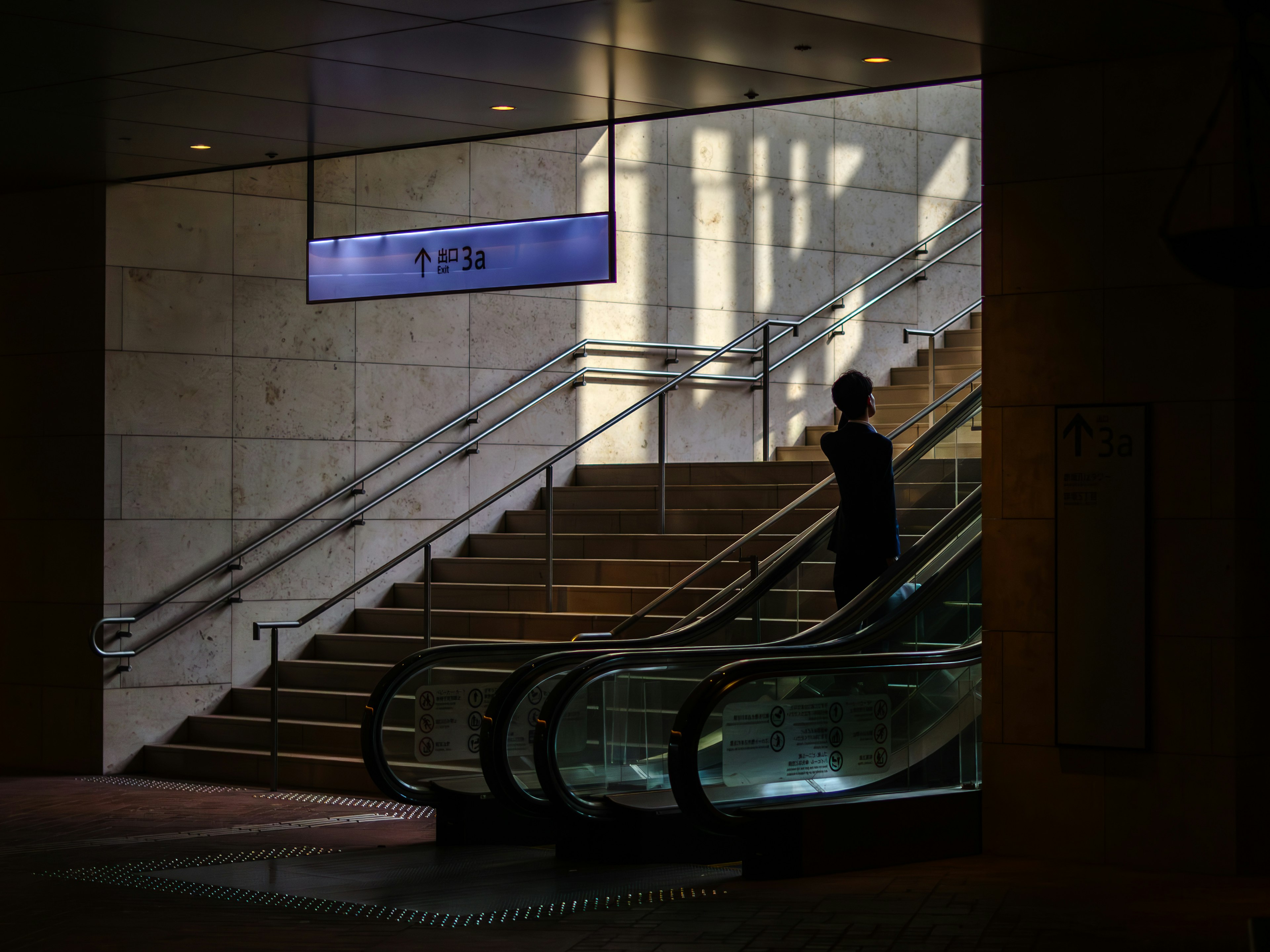 Silhouette di una persona in piedi in un interno moderno di una stazione con scale e scale mobili