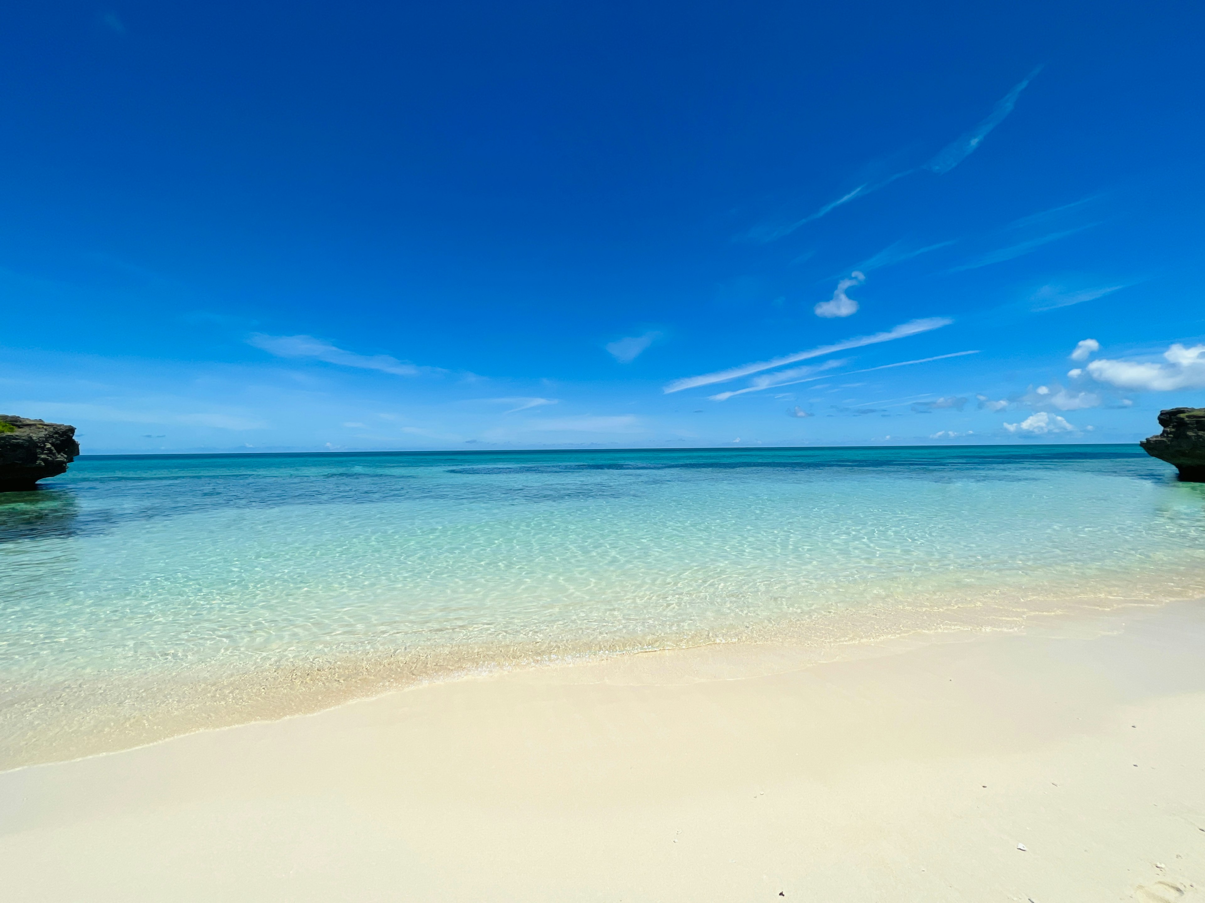 Pantai dengan air jernih dan langit biru pasir dan garis pantai berbatu