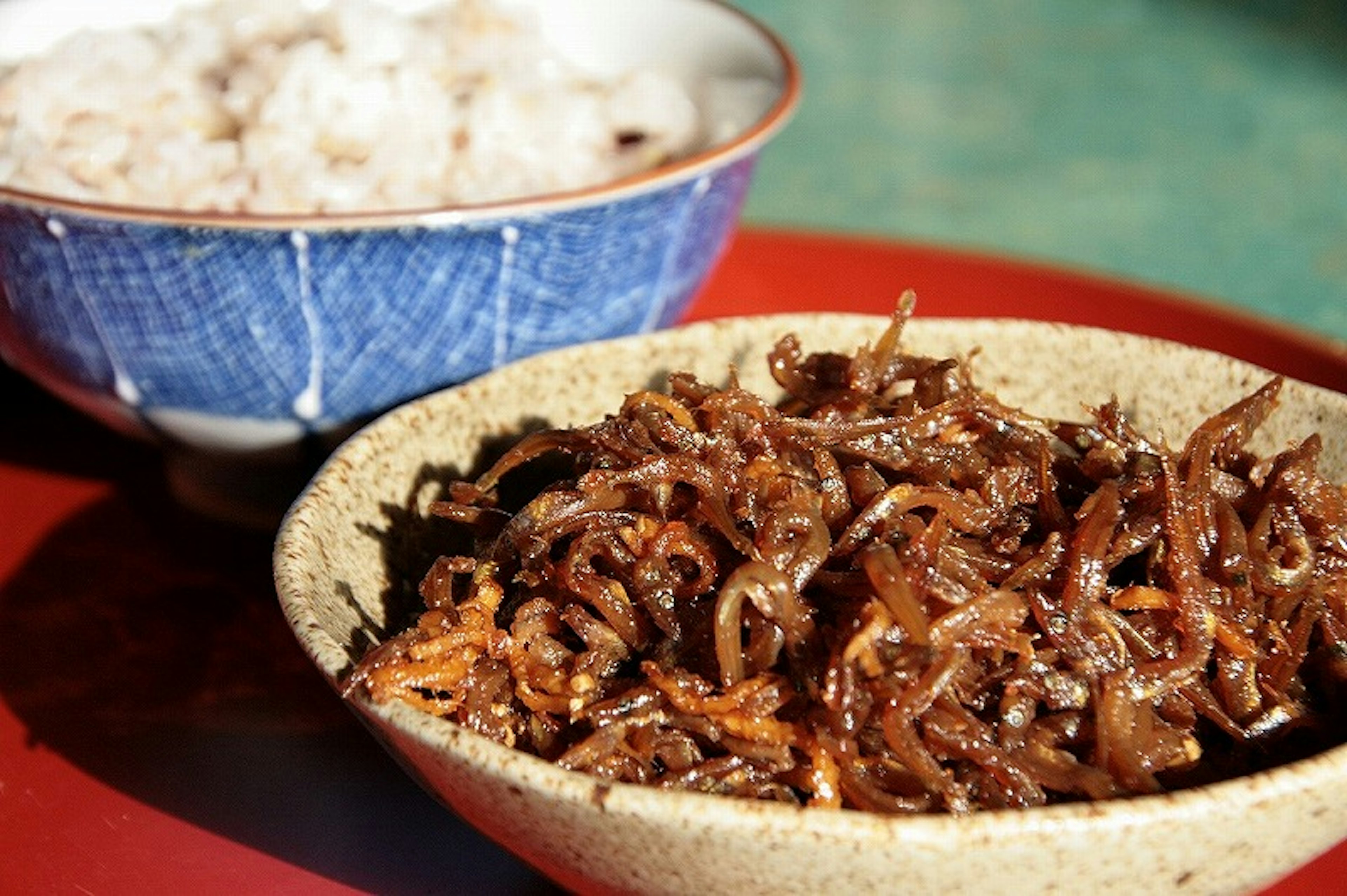 Un tazón de arroz junto a un plato de tsukudani de algas dulces y saladas