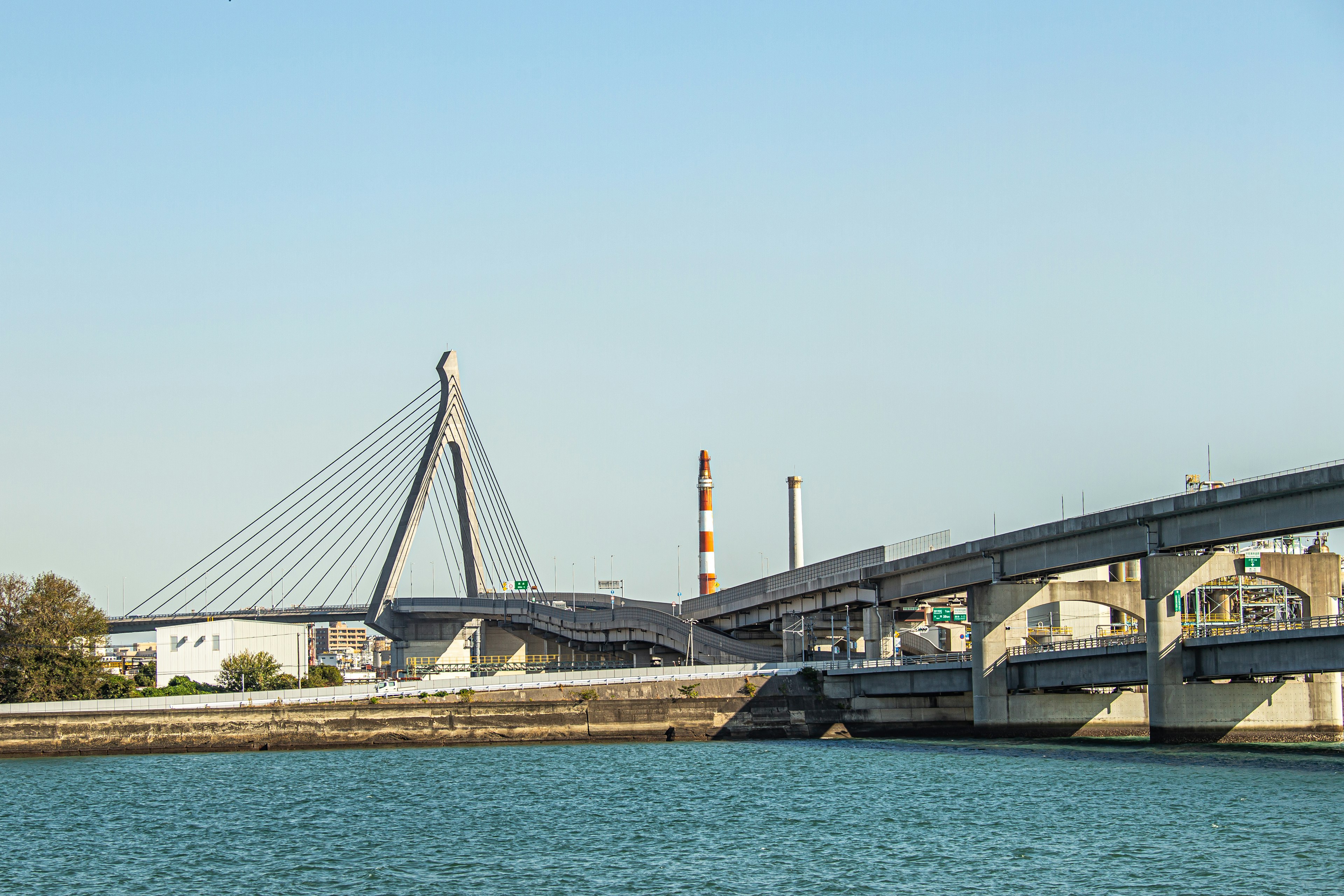 Modern cable-stayed bridge alongside a river with industrial buildings