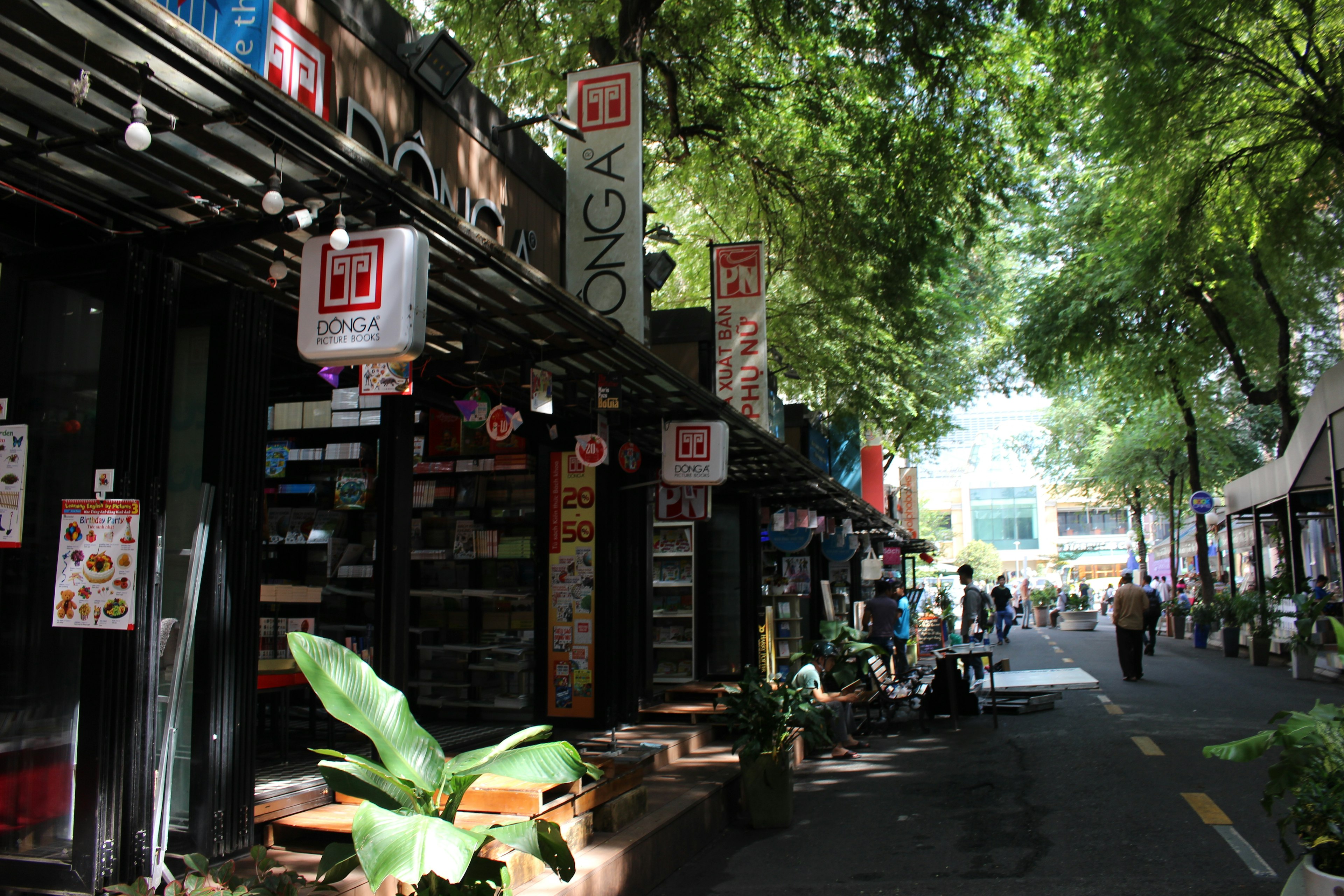 Lively street scene with shops and people under lush green trees