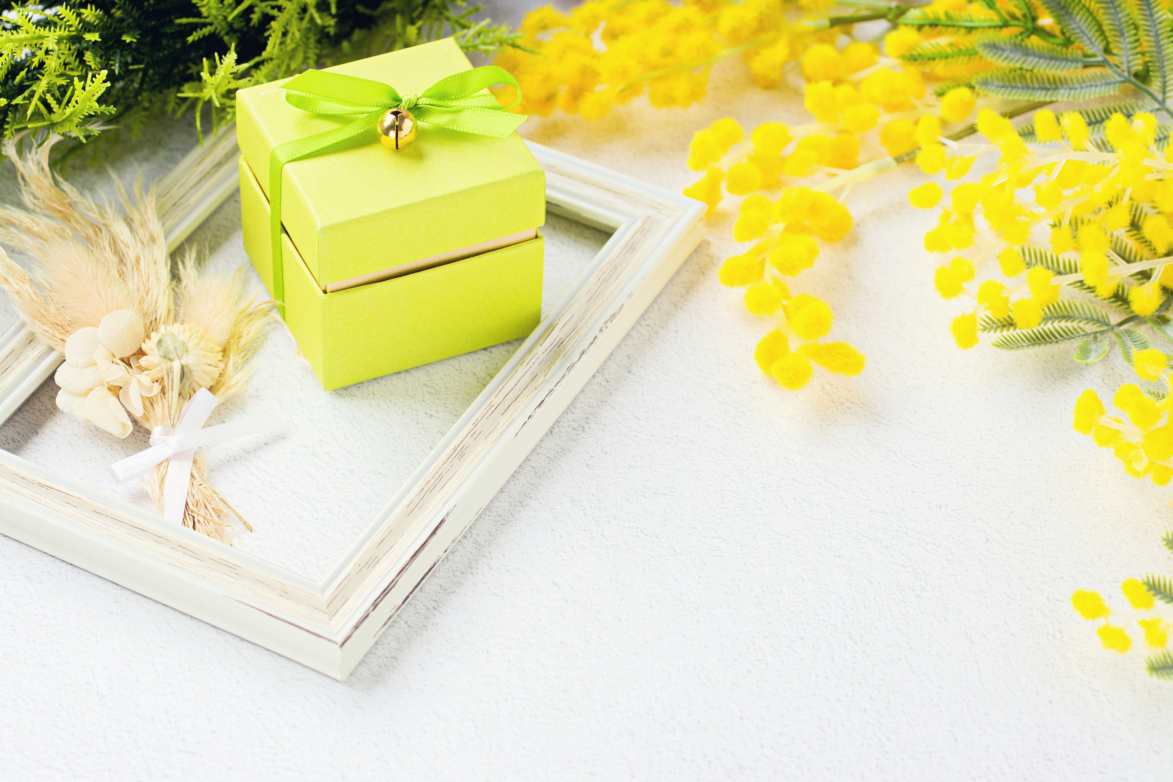 Pequeña caja de regalo verde con una cinta rodeada de flores amarillas y un marco decorativo