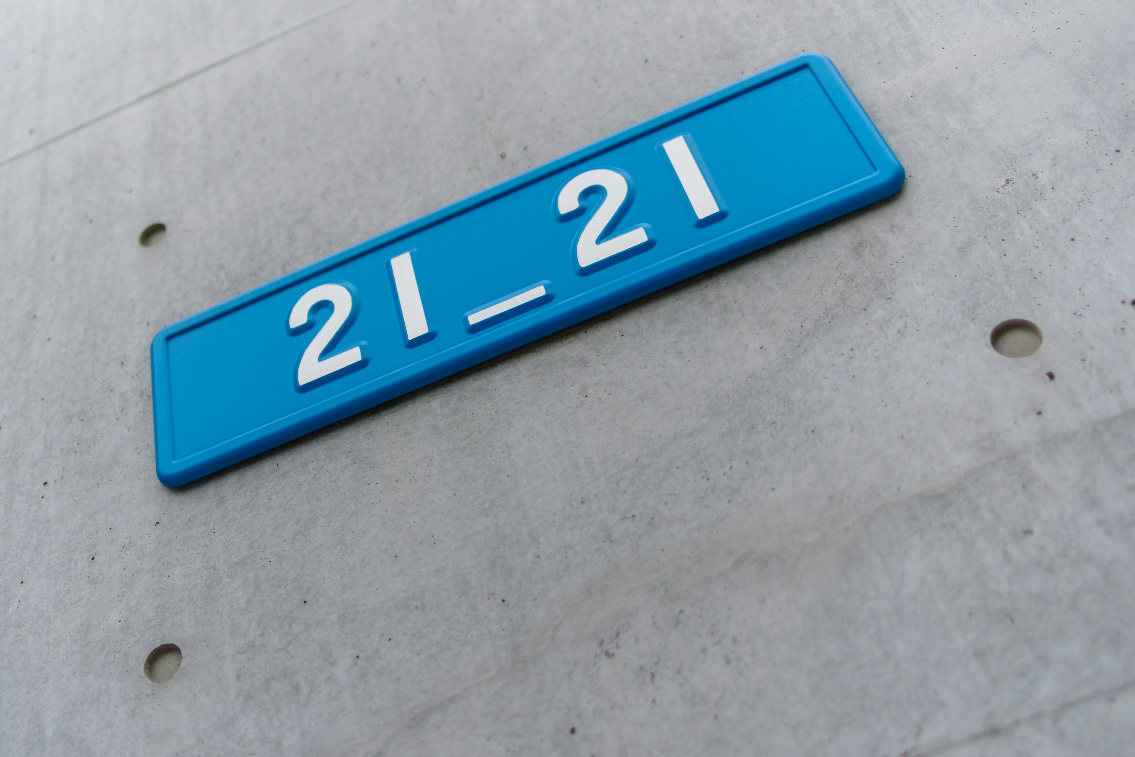 A blue sign displaying the number 21_21 mounted on a concrete wall