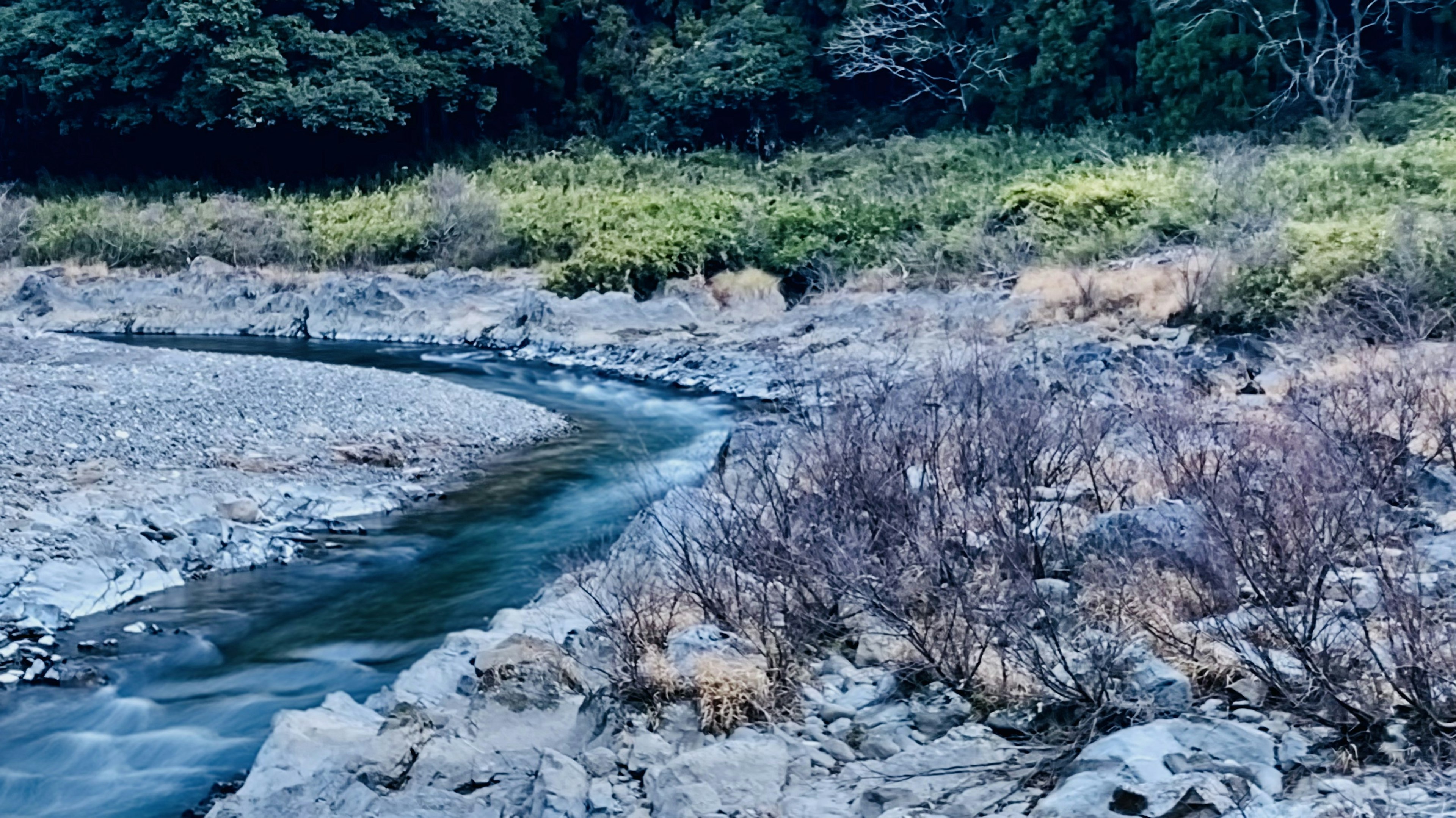 Ruhiger Bach, der sich durch felsige Ufer und spärliche Vegetation schlängelt