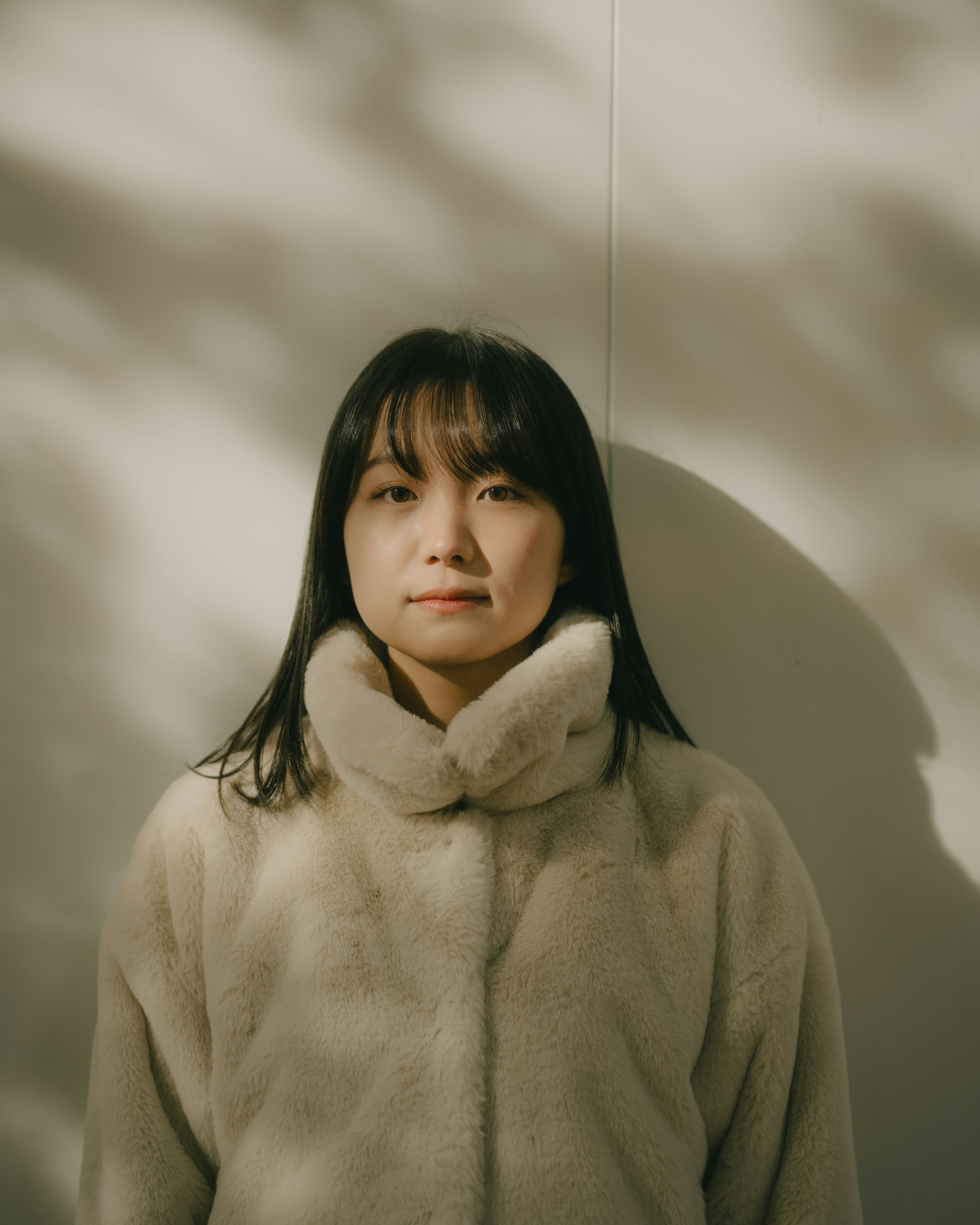 Woman in a soft fur coat standing against a wall