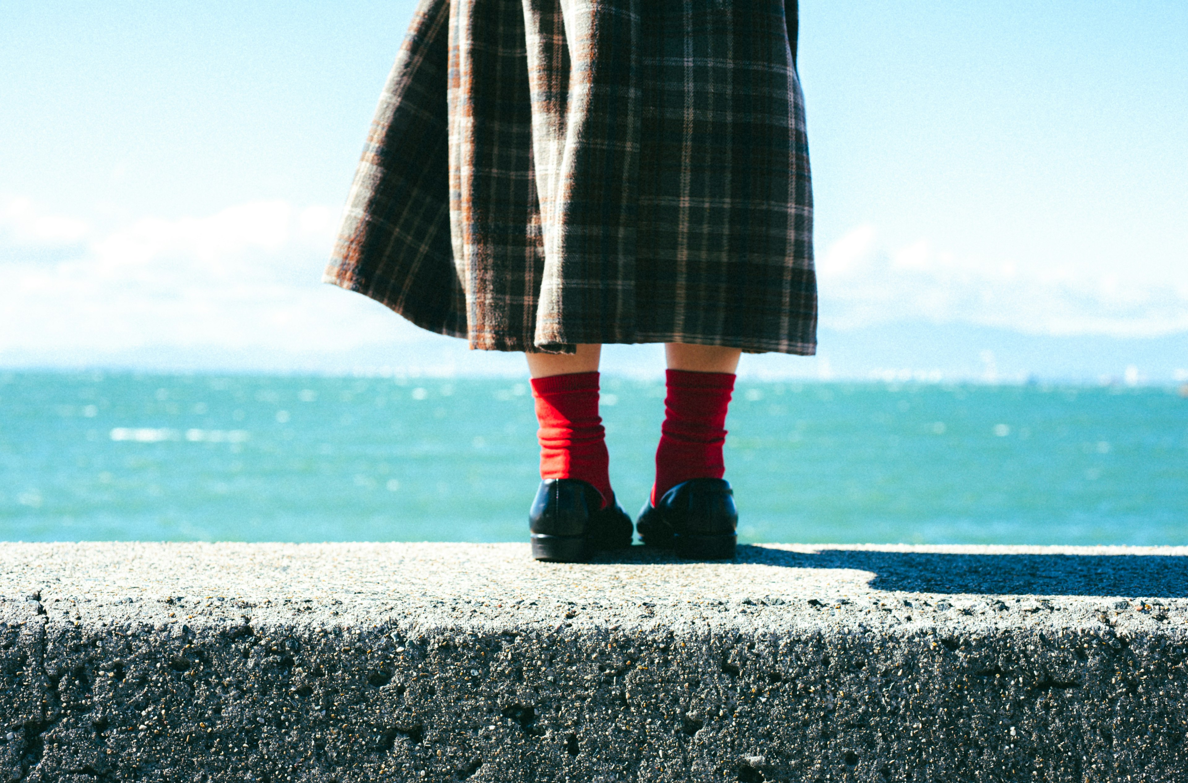 Una persona de pie junto al mar con una falda de cuadros y calcetines rojos