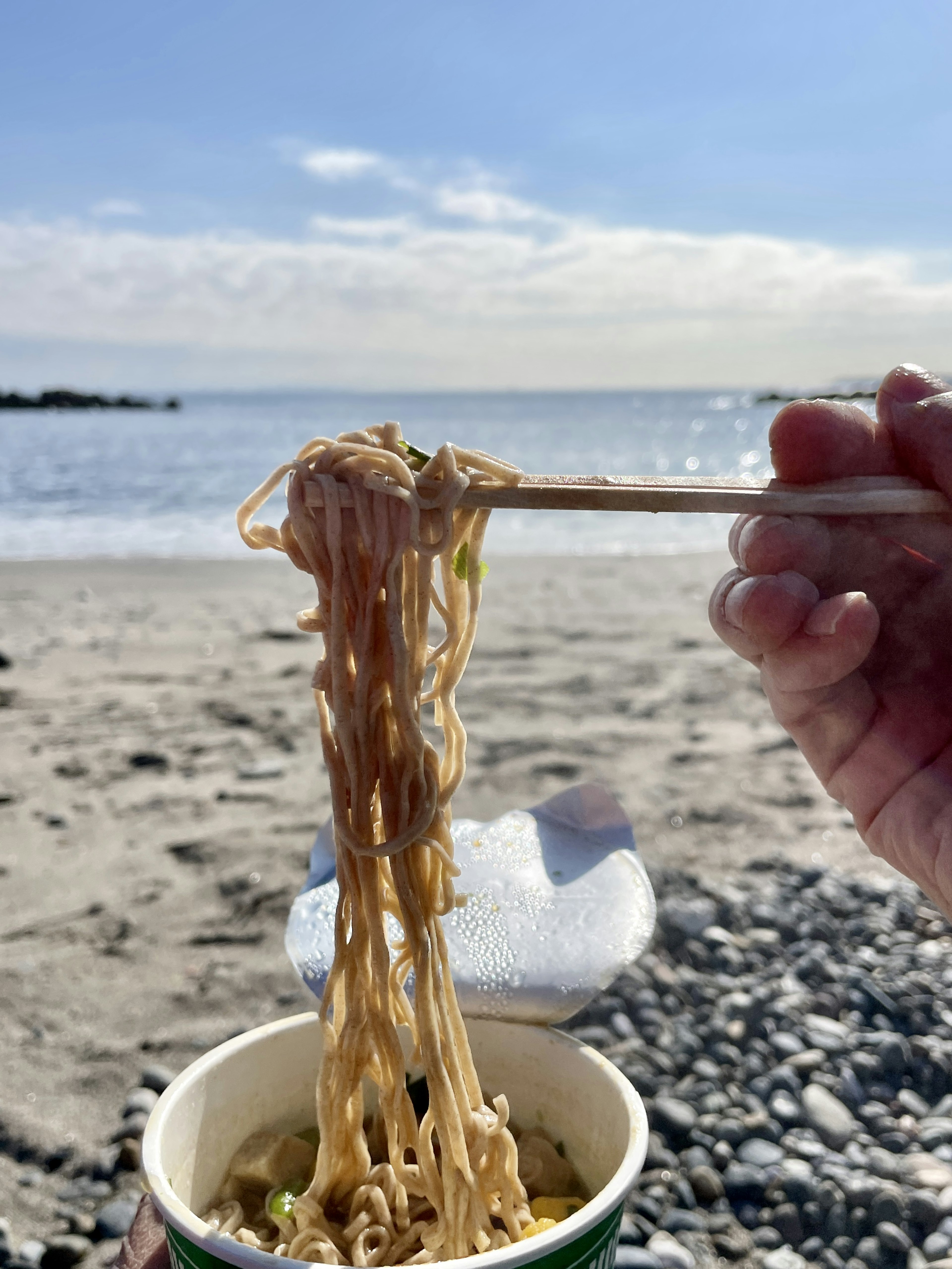 手在海滩上拿着杯子里的面条，背景是海洋