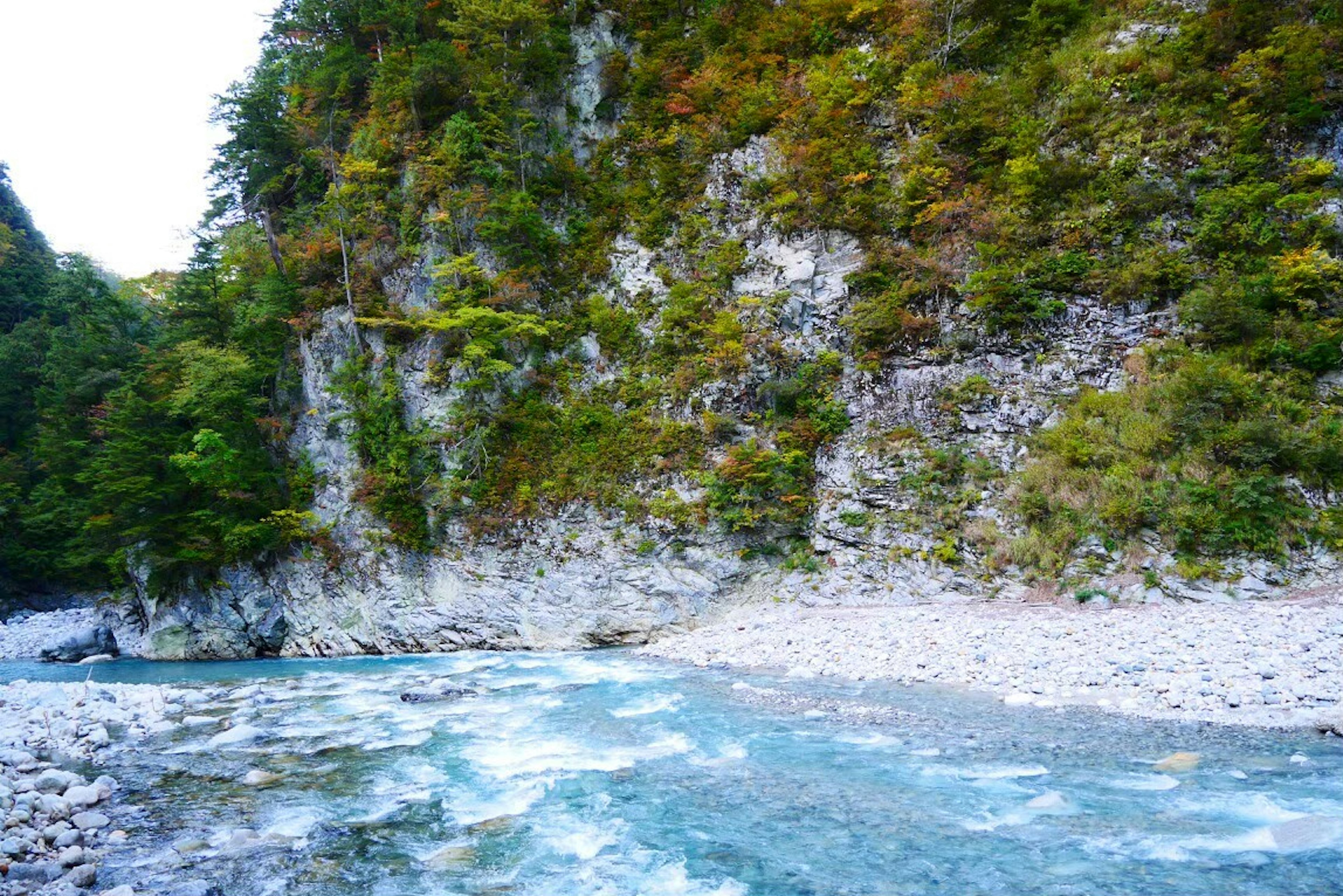 Pemandangan indah sungai biru dikelilingi pepohonan hijau dan tebing berbatu