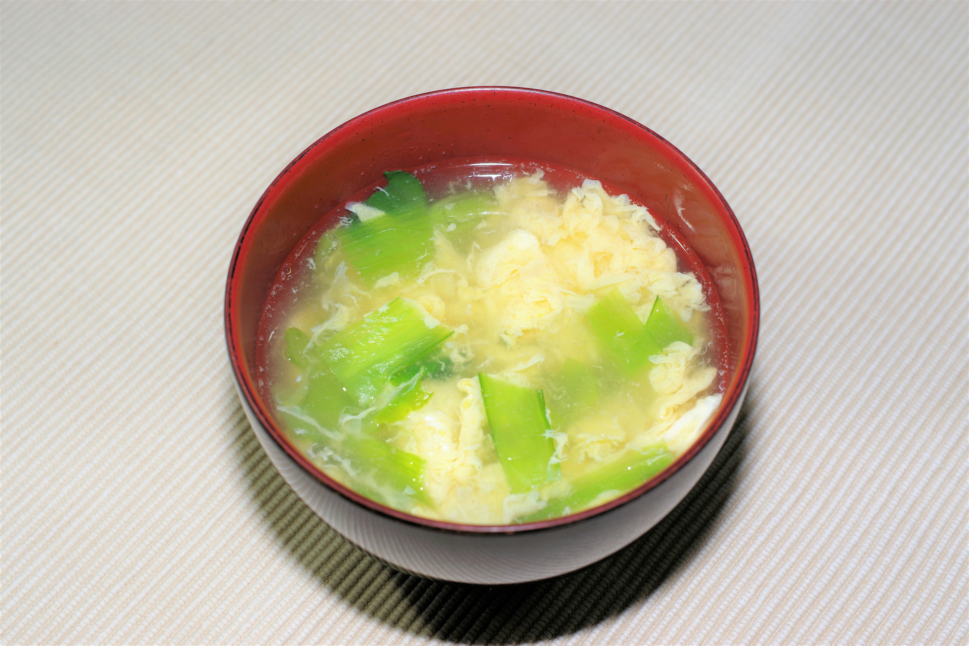 Red bowl of soup with green vegetables and egg