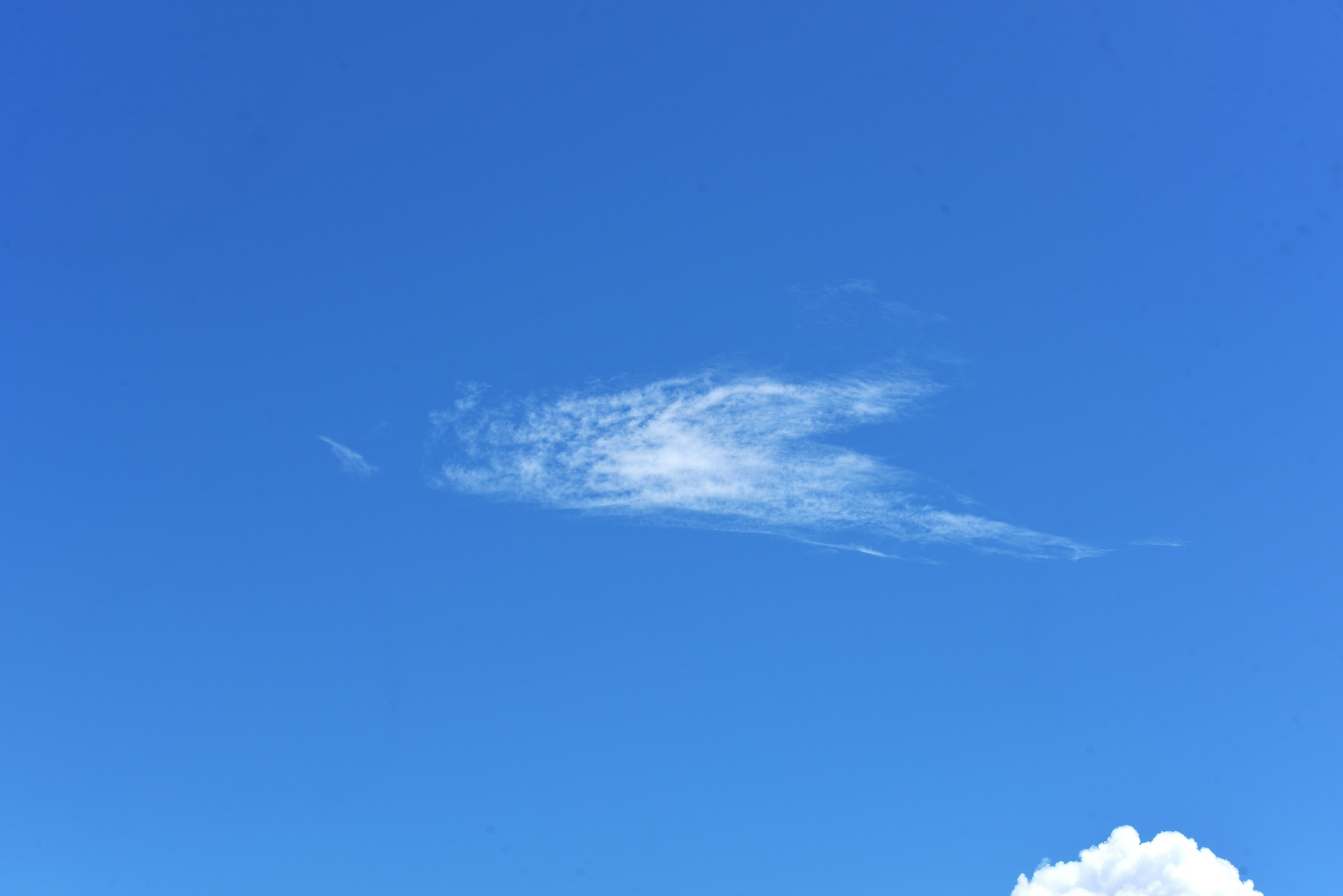 Eine dünne Wolke schwebt in einem klaren blauen Himmel mit einem Teil einer weißen Wolke