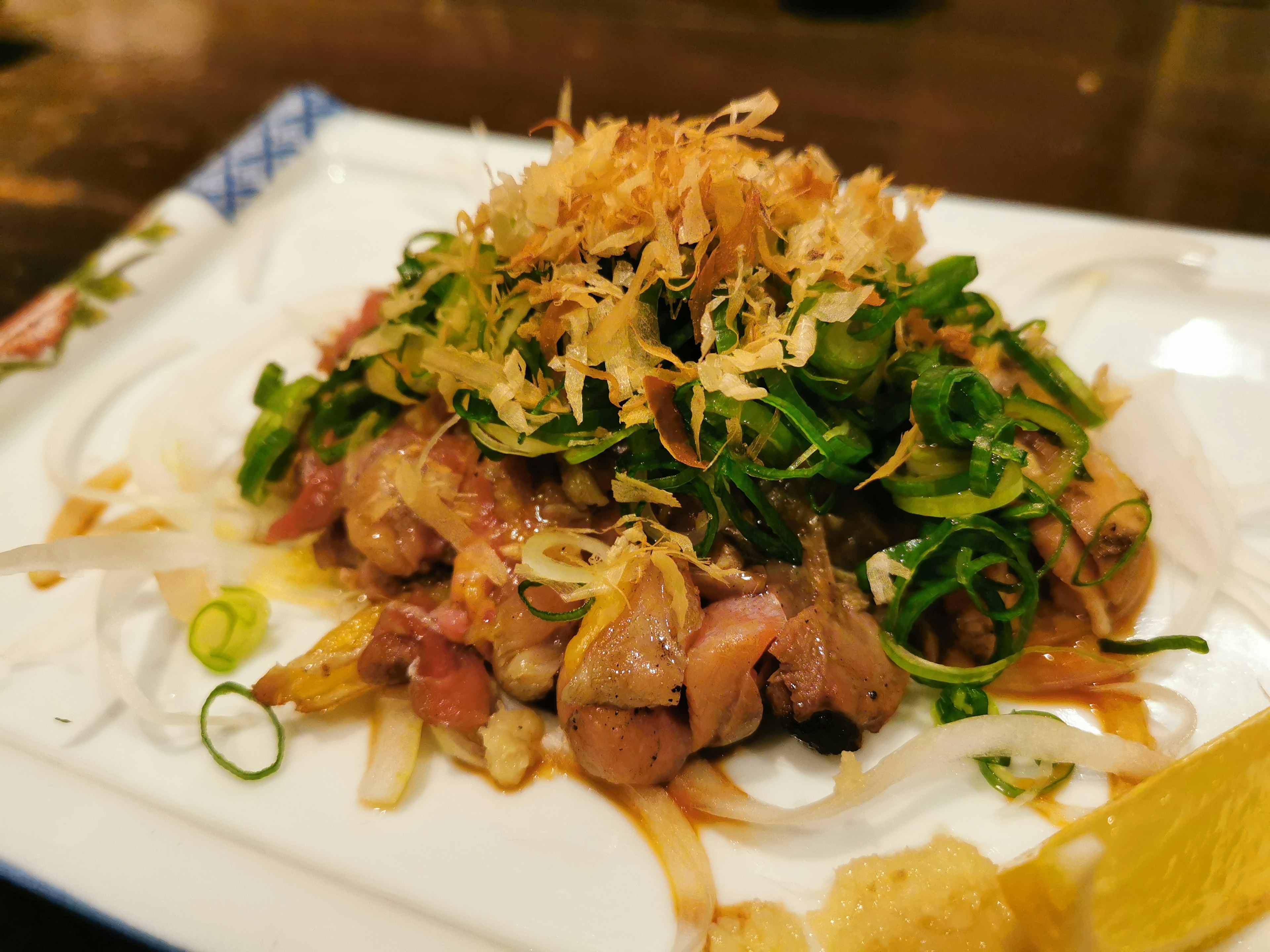 Un plato con carne fresca cubierta de hierbas y cebollas crujientes