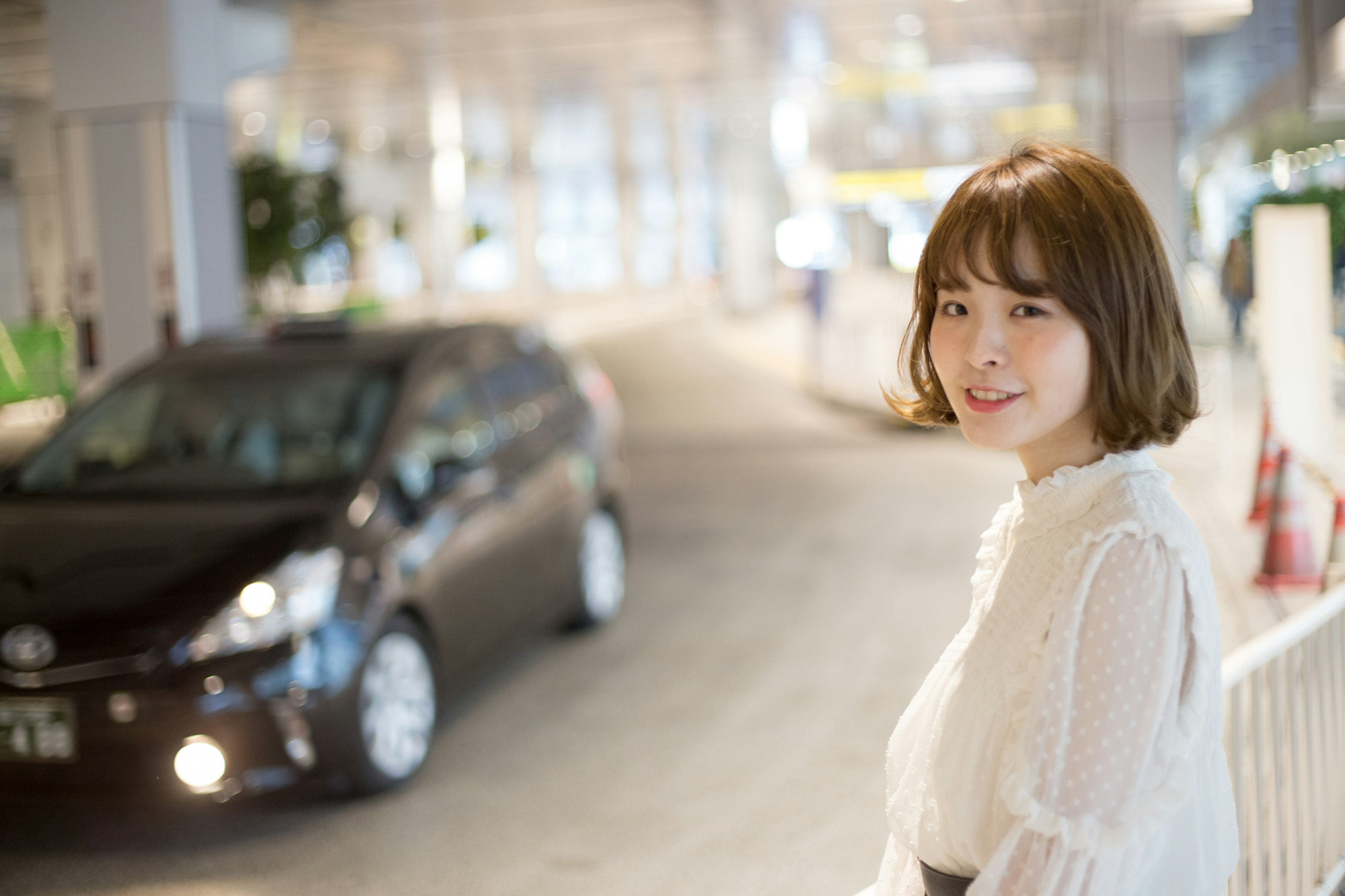 Young woman in a white blouse smiling with a car in the background