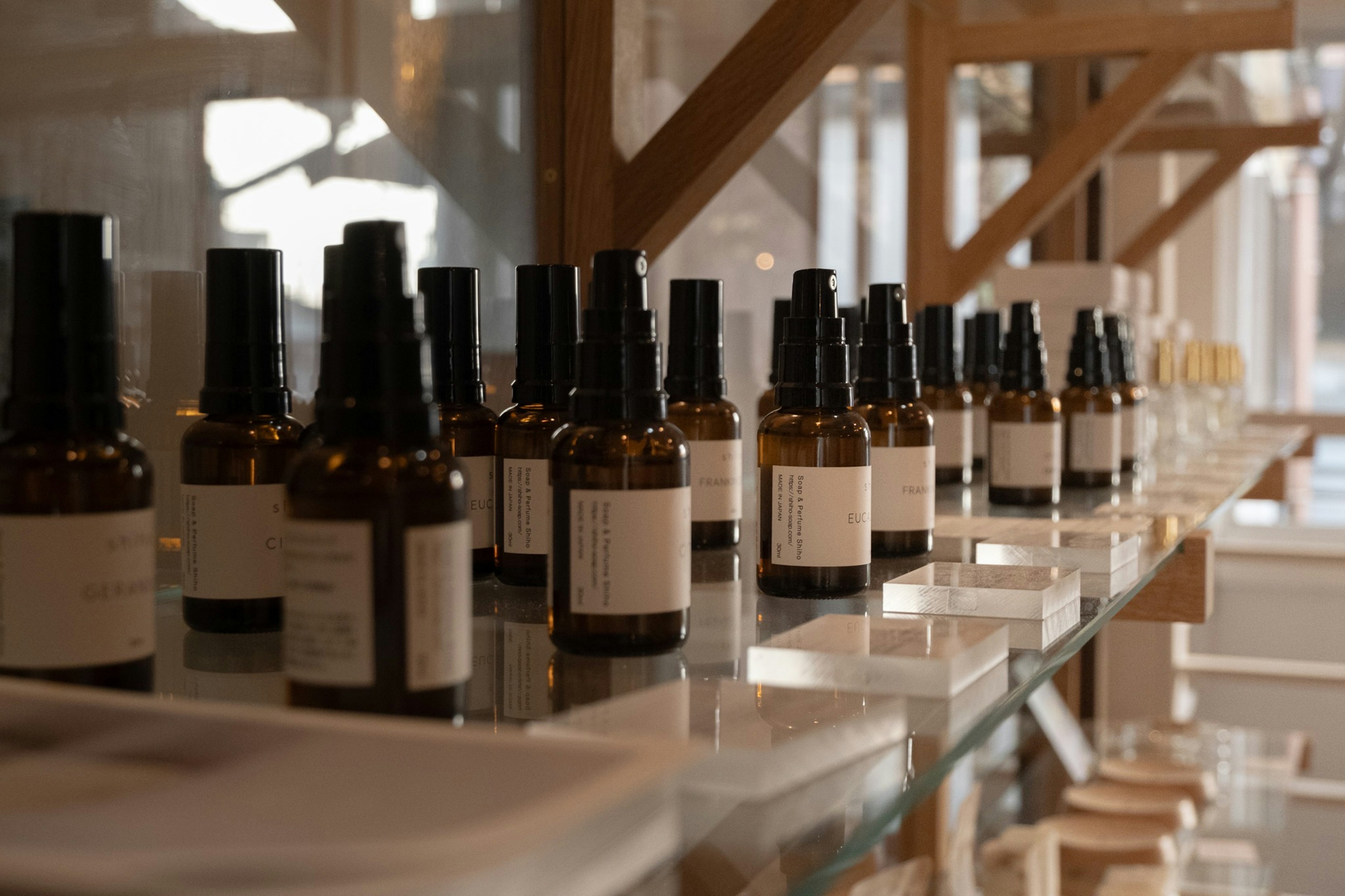 Row of brown bottles with white labels on a clear shelf in a well-lit space