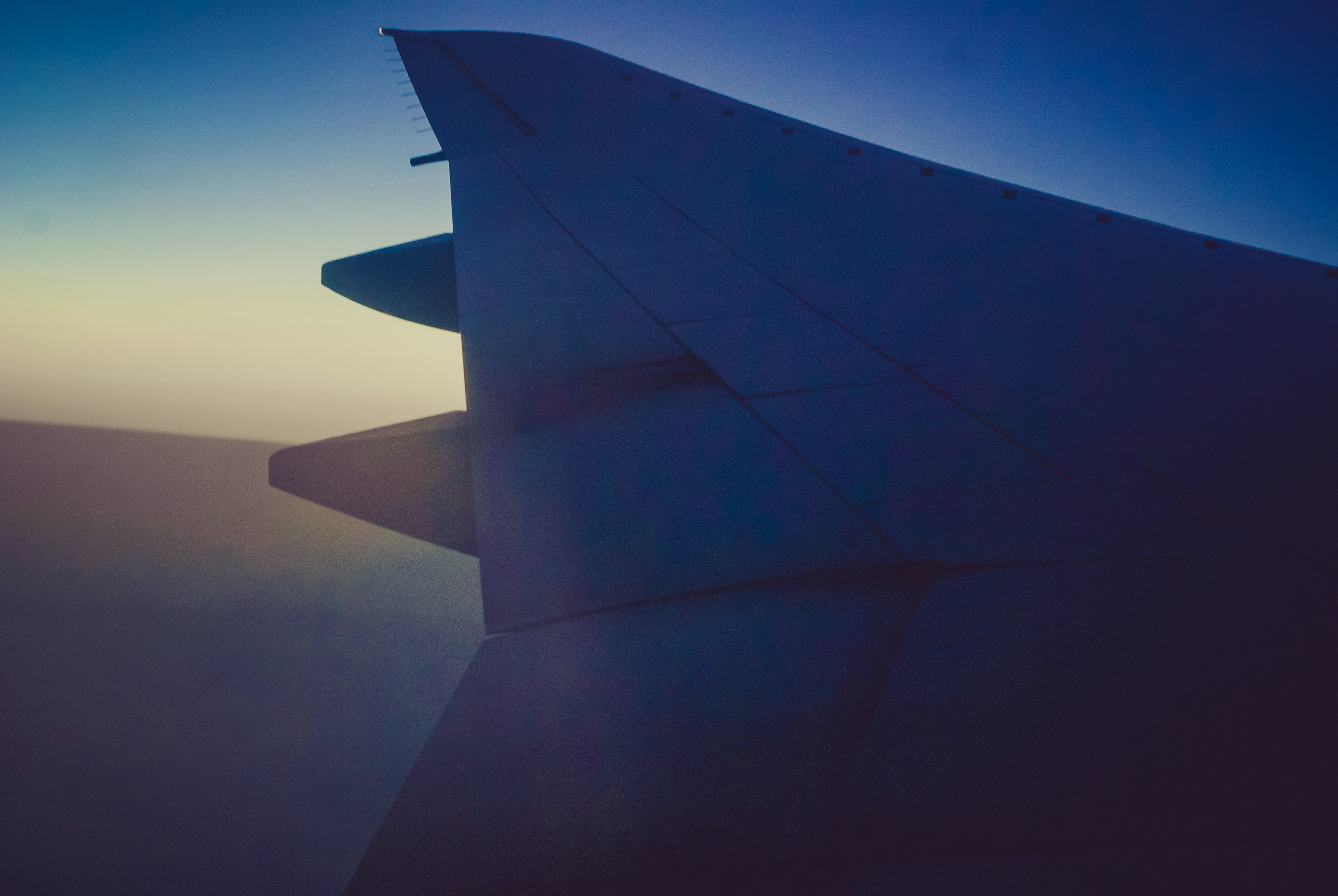 Silhouette of an airplane wing against a gradient of blue and purple sky