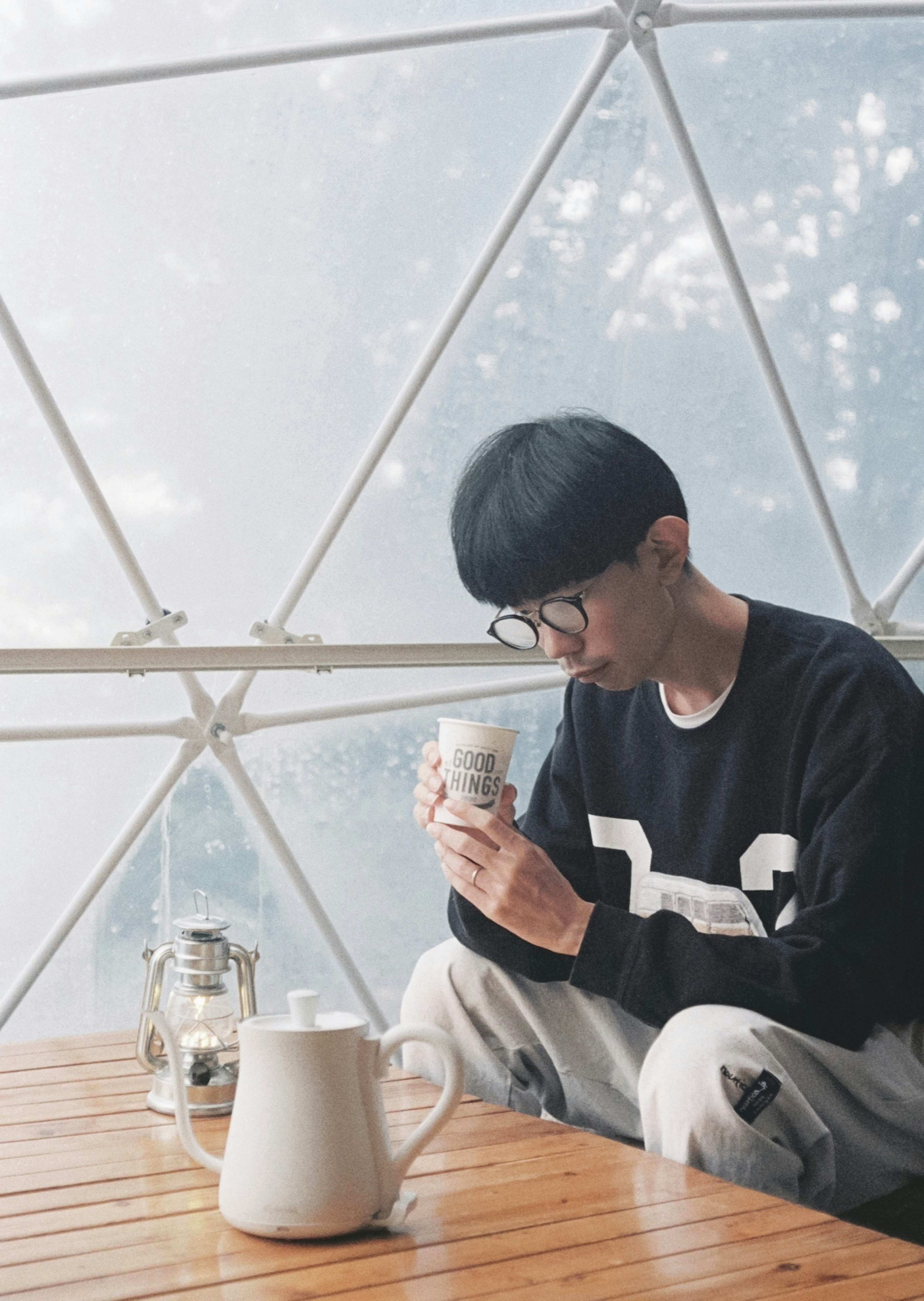 Young person sitting in a transparent dome holding a coffee cup