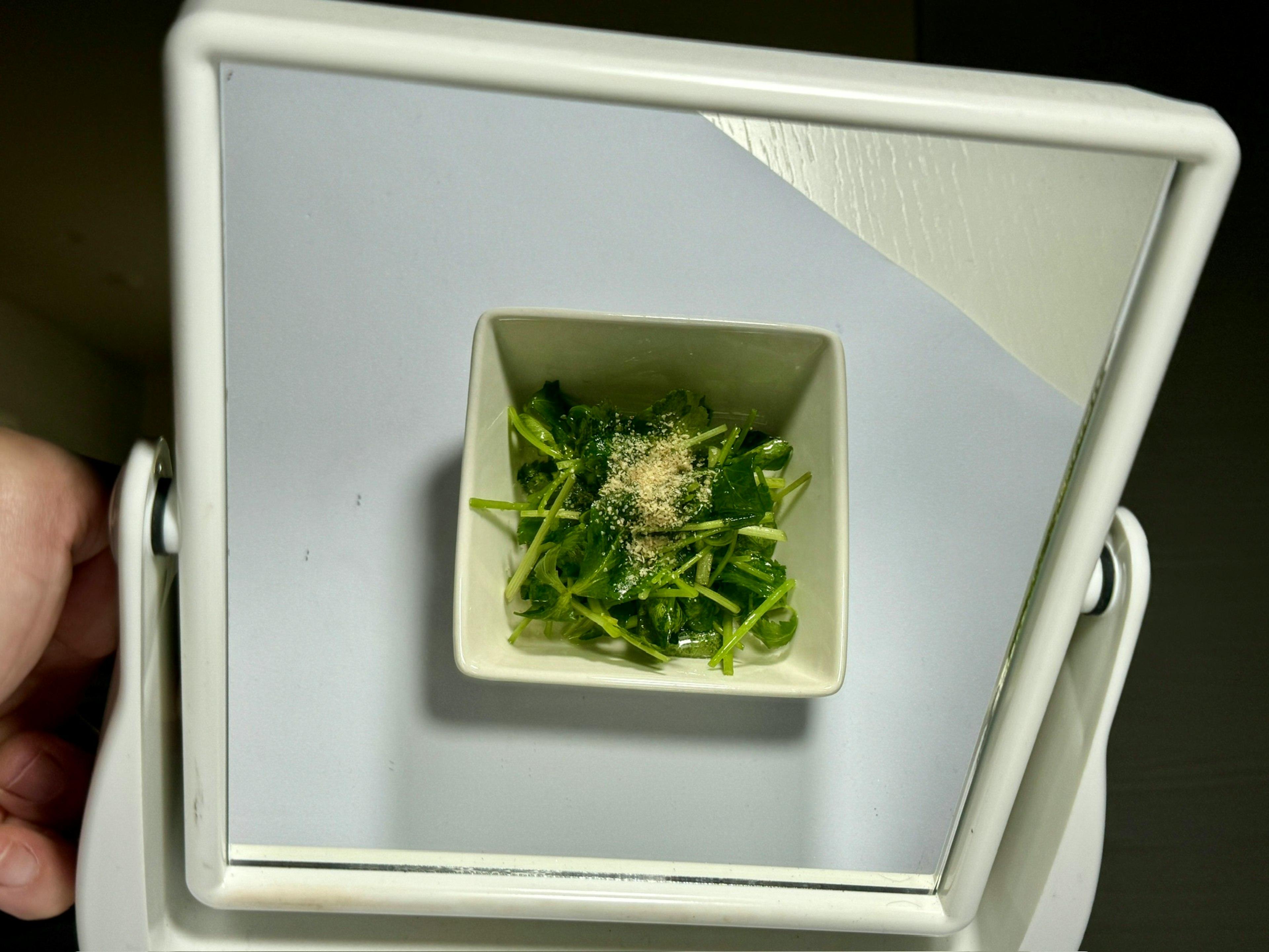 Fresh leafy greens in a small white container with a sprinkle of seasoning