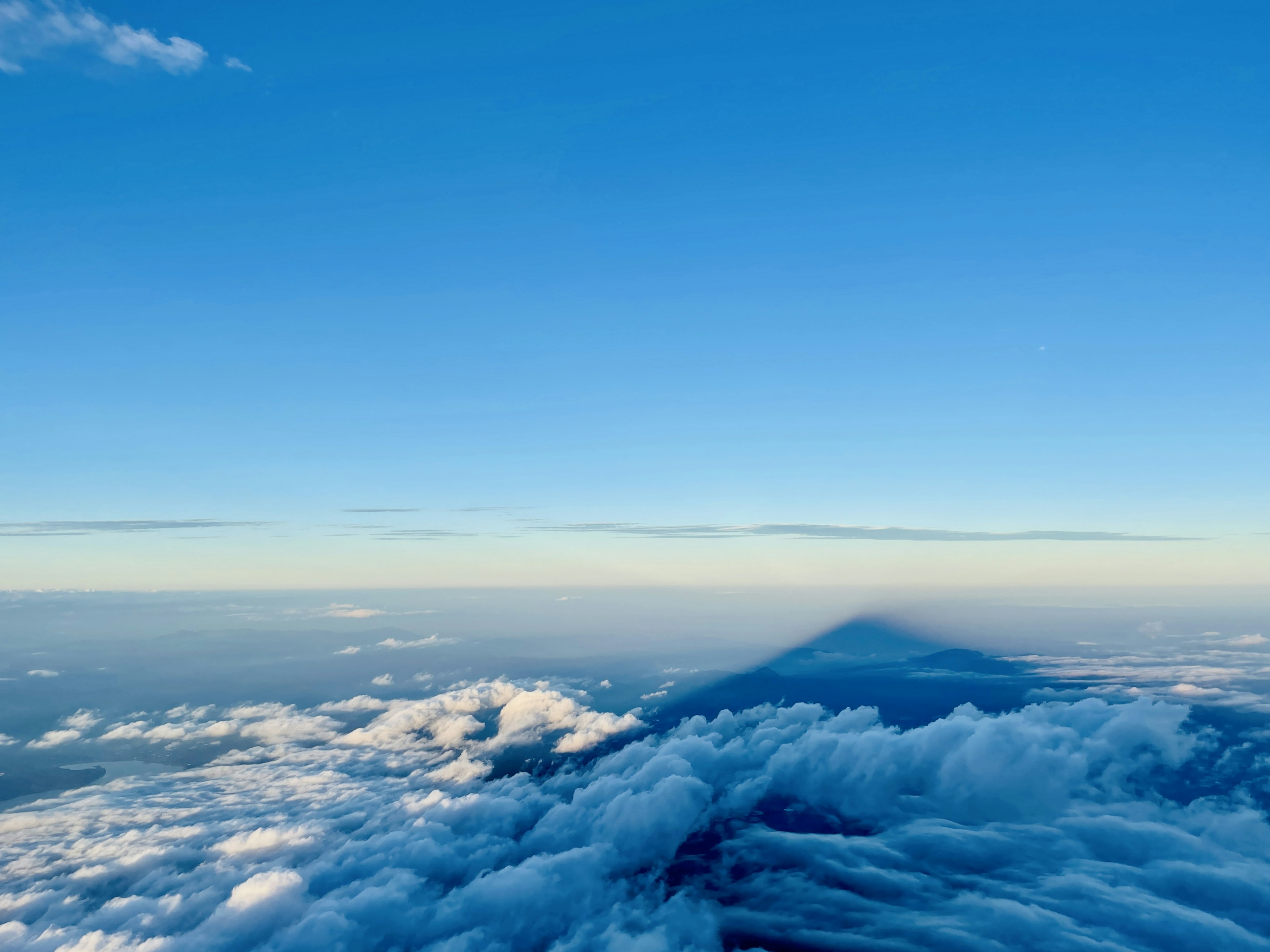 Sombra de una montaña proyectada sobre nubes bajo un cielo azul claro