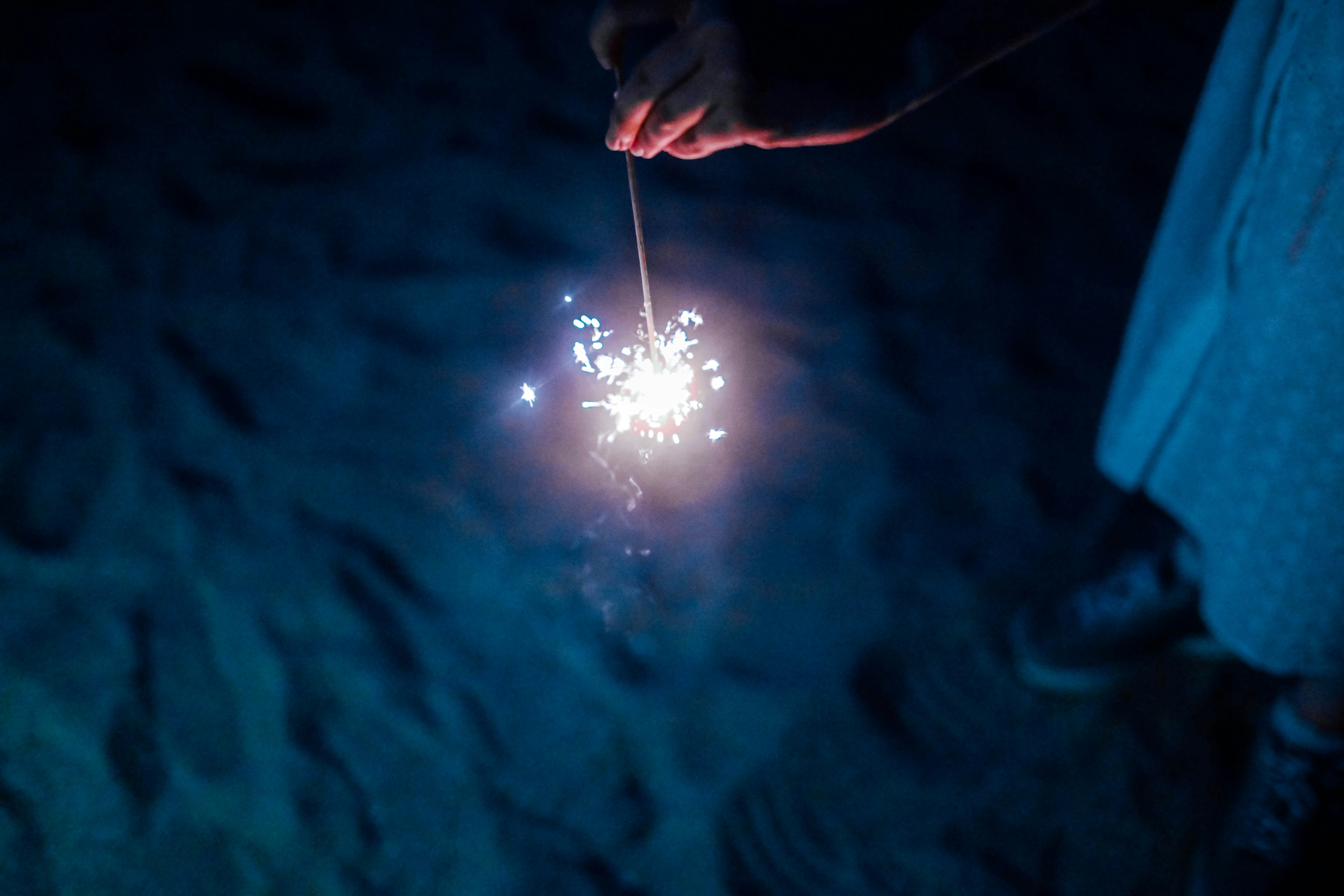 Mano sosteniendo un fuego artificial que emite chispas brillantes contra un fondo oscuro