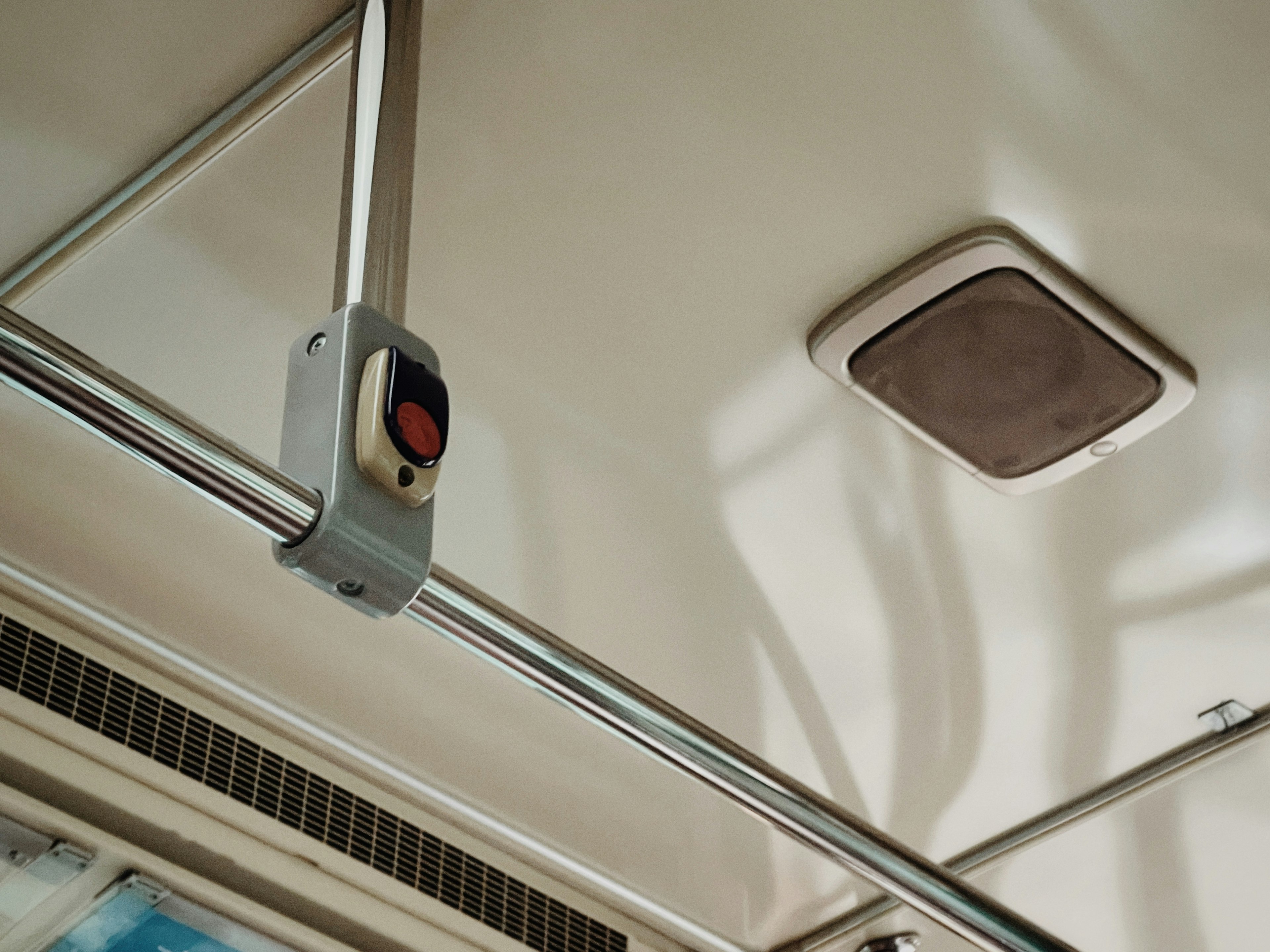 Interior de un transporte público con pasamanos en el techo y un botón rojo