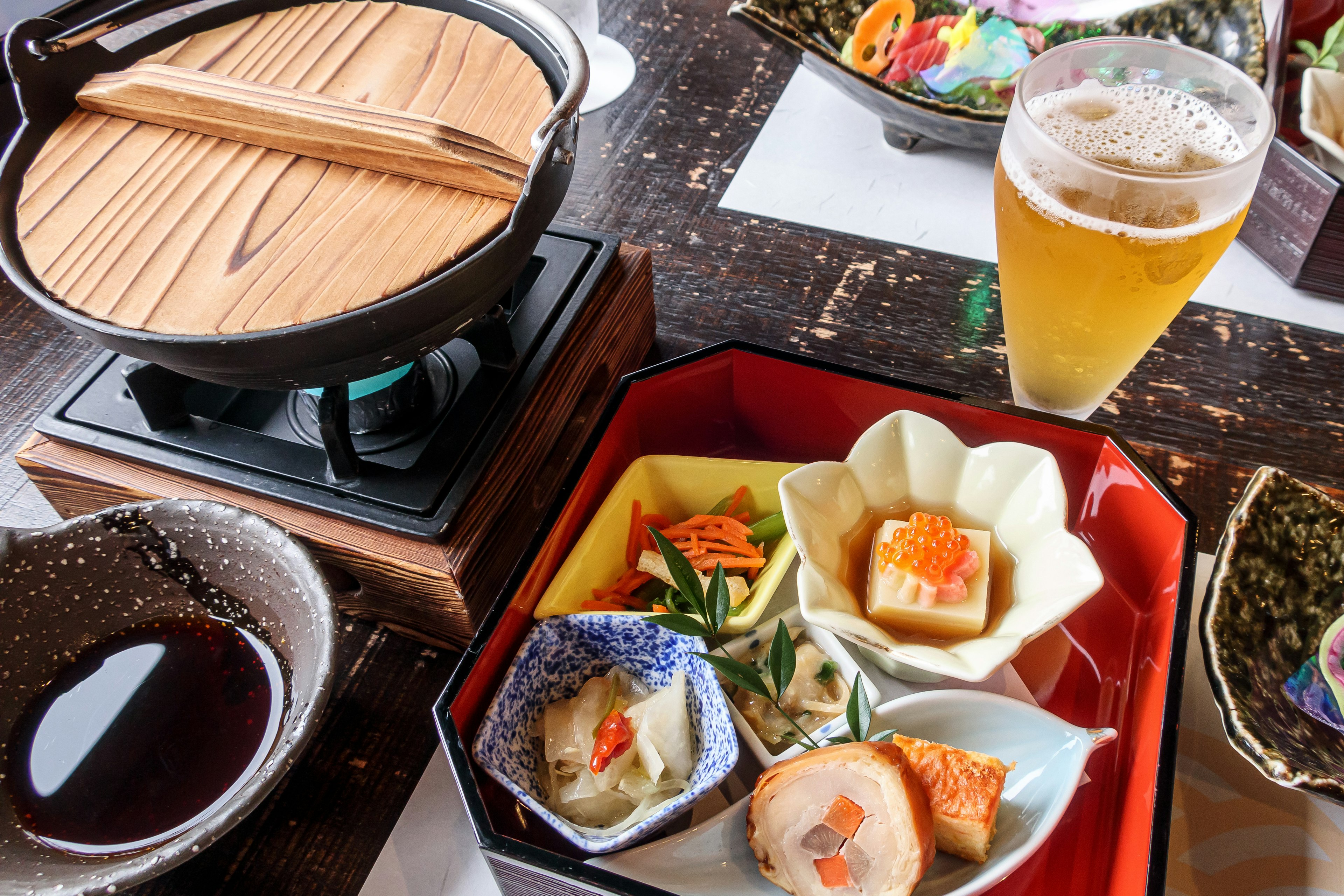 Ein japanisches Küchenarrangement mit Bier, das einen heißen Topf und verschiedene Gerichte zeigt